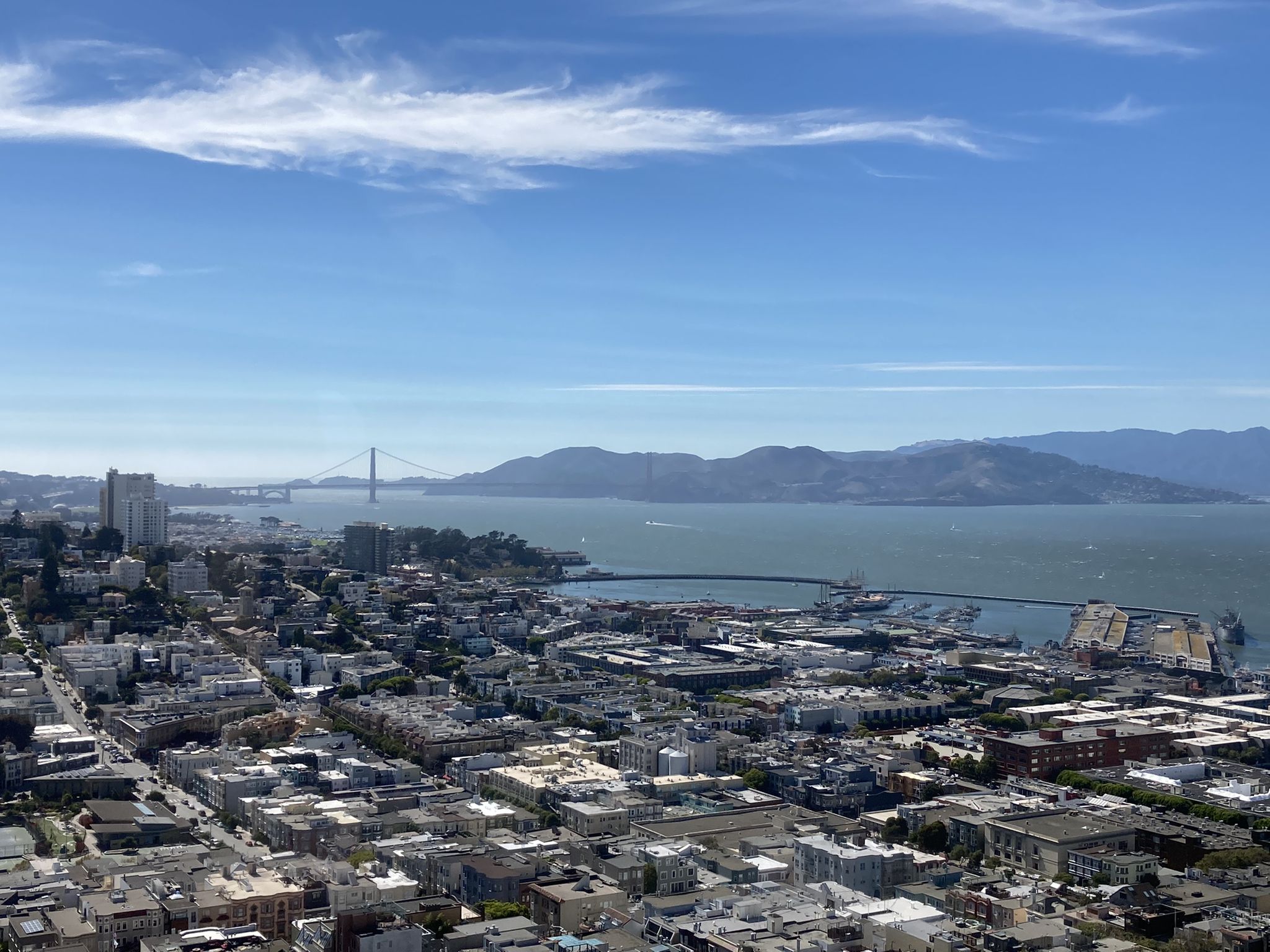 Aerial view of a city, bay, distant bridge, and mountains under a blue sky. - Filbert Steps to Telegraph Hill Hike