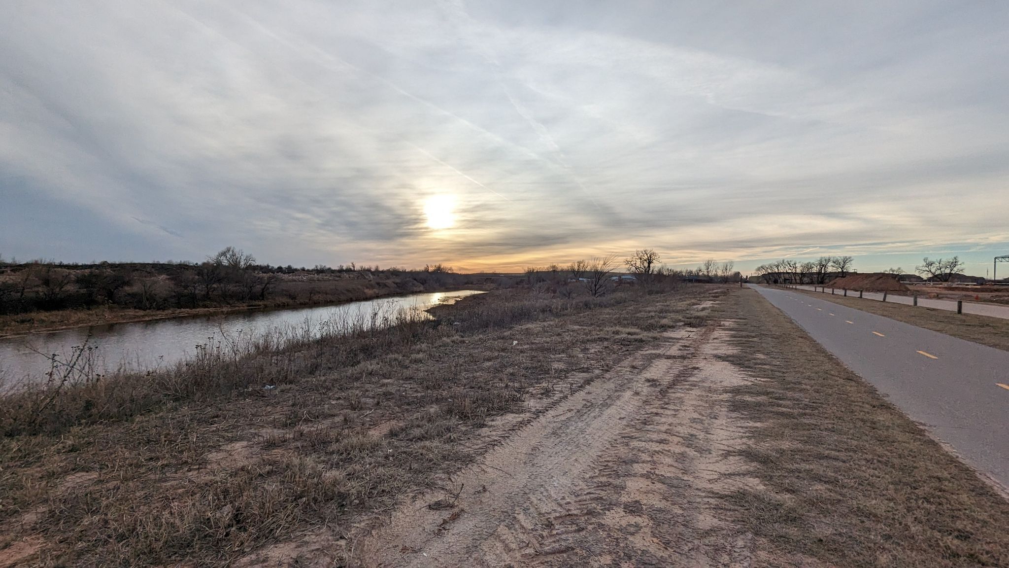 Sunset over a river next to a dirt path and paved trail. - West River Trail