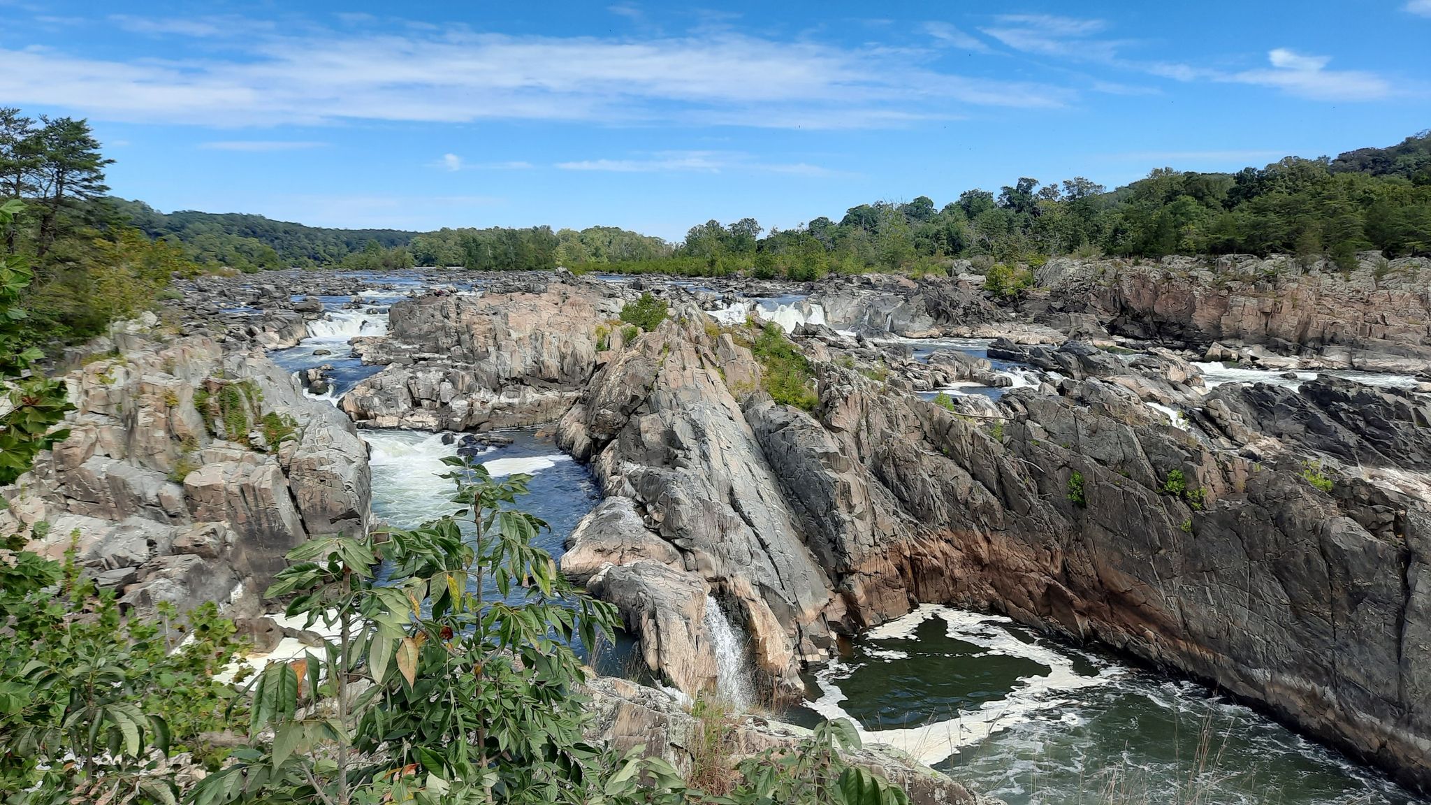 Panoramic view of a wide river with rocky outcrops and small waterfalls under blue sky. - Potomac Heritage Trail