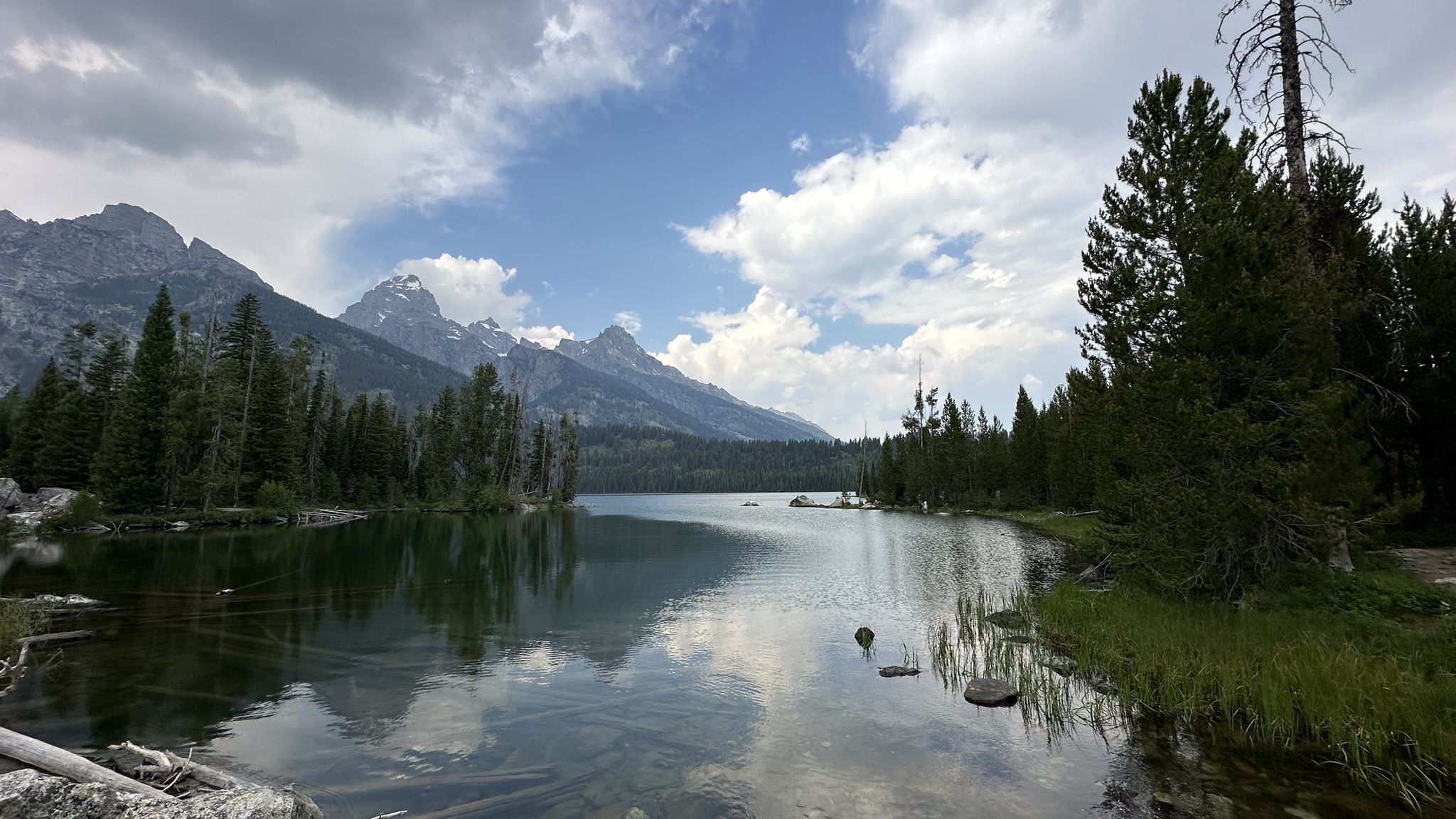 Calm lake reflecting mountains and trees under a partly cloudy sky. - Taggart Lake-Bradley Lake Loop