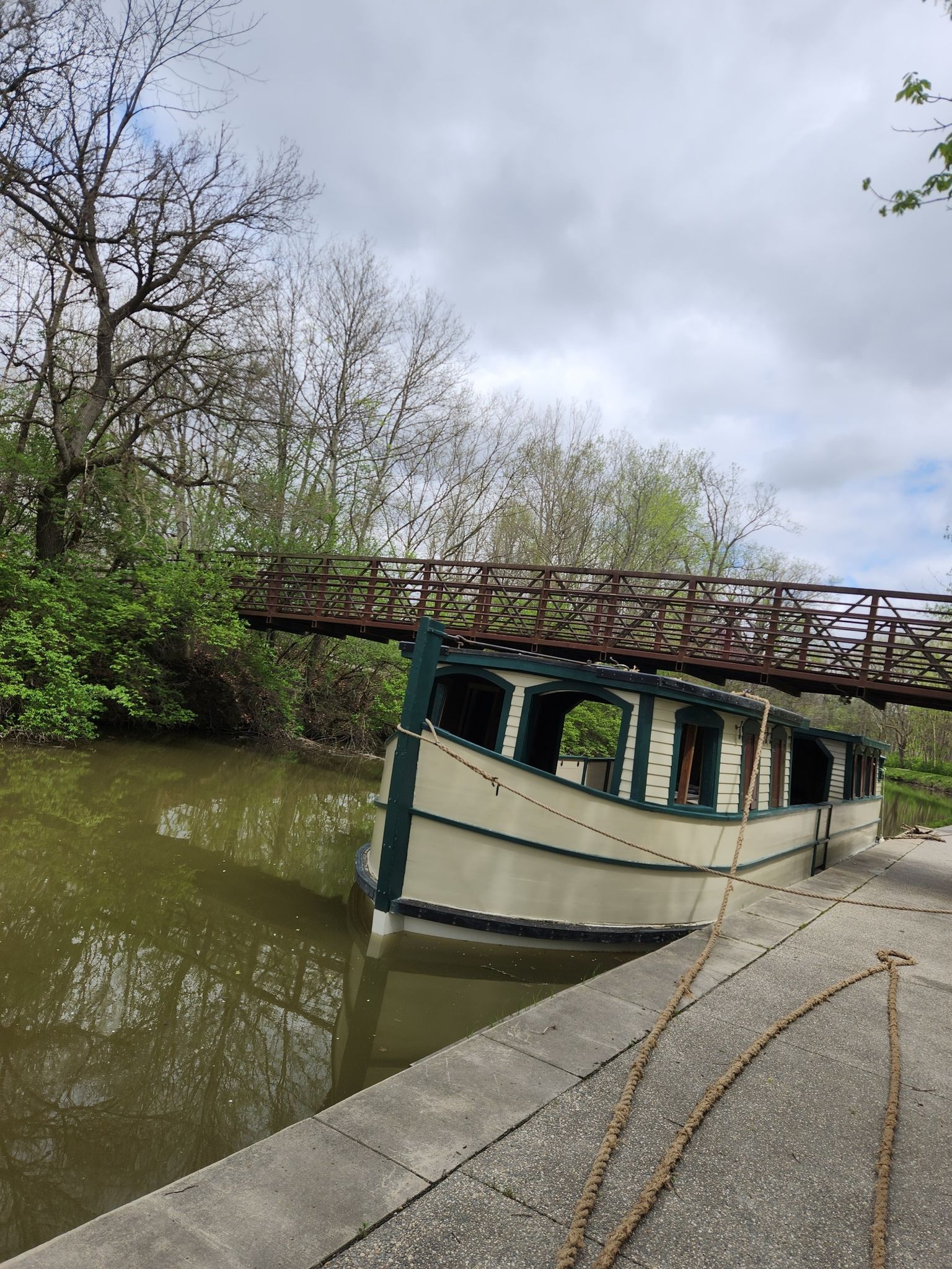 A historic canal boat is docked beside a pedestrian bridge on a cloudy day. - Farnsworth Metropark – Towpath Trail loop from Otsego