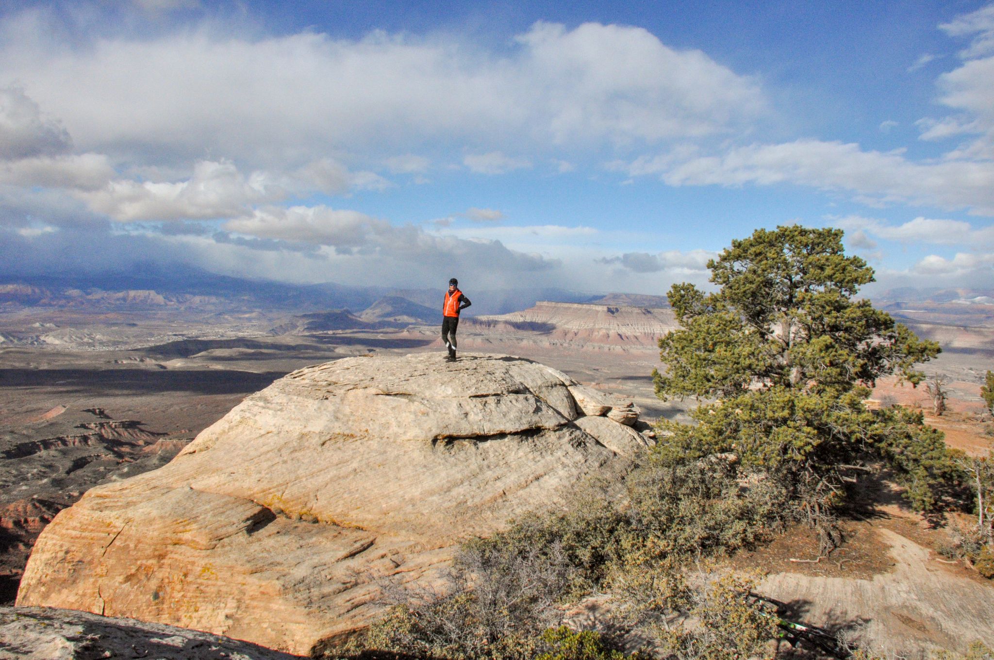Person stands on a large rock overlooking a vast desert landscape. - North Rim Trail – Gooseberry Point loop from Gooseberry Mesa Trailhead