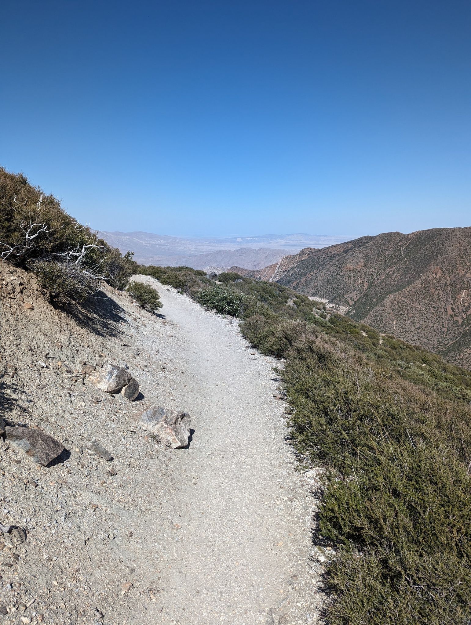 Narrow dirt trail winding along a steep mountain ridge overlooking a vast valley. - Garnet Peak via PCT
