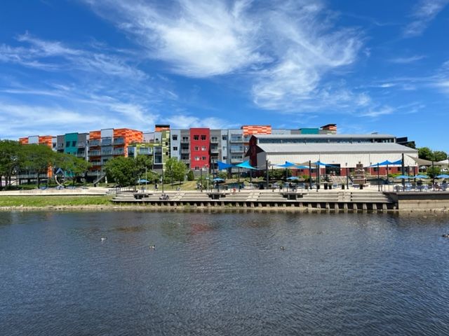 Colorful buildings line a sunny waterfront with blue sky and clouds. - Lansing River Trail to South Lansing Pathway