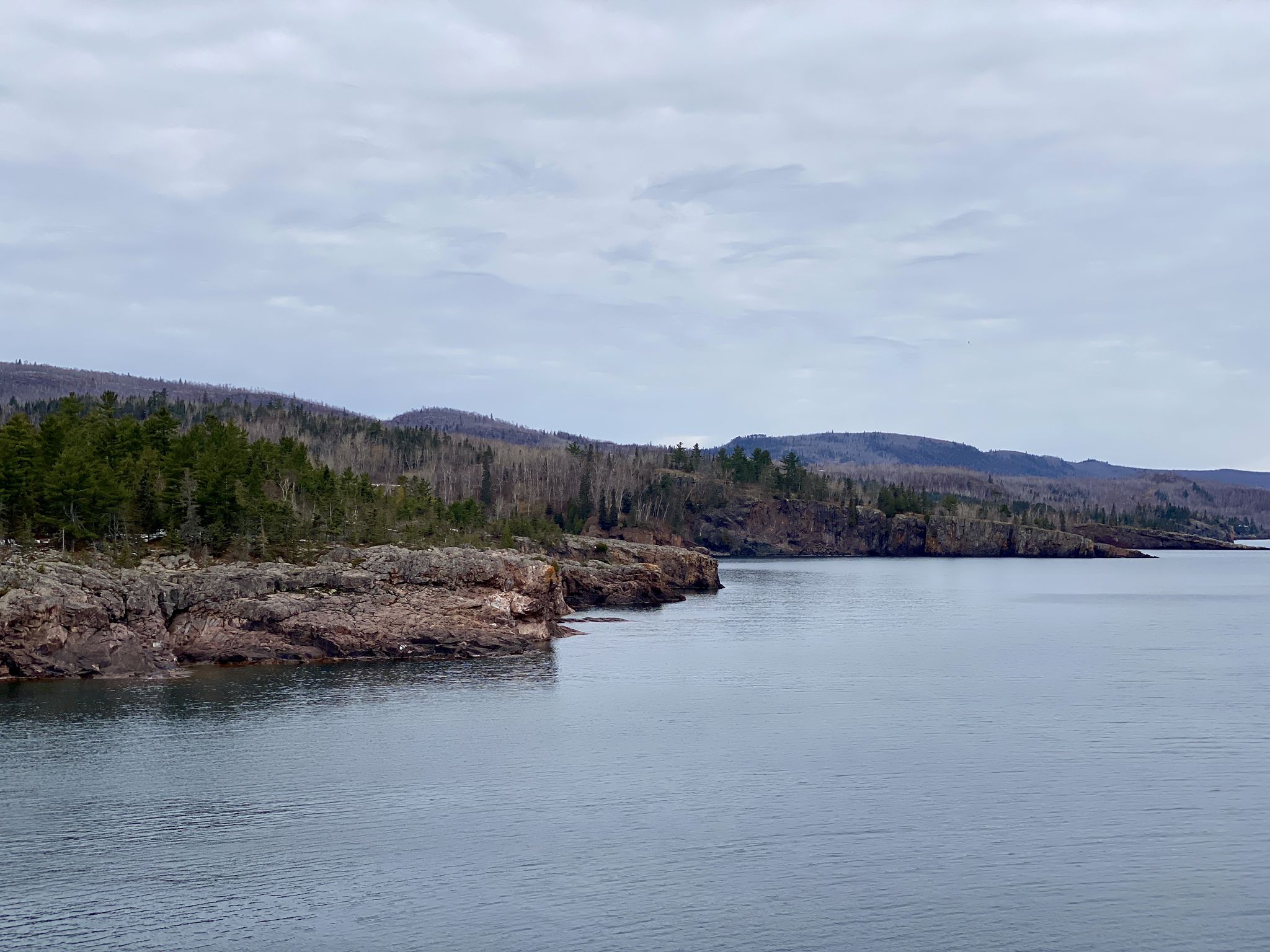 Cloudy day over a large body of water with rocky, forested shorelines. - Shovel Point Trail