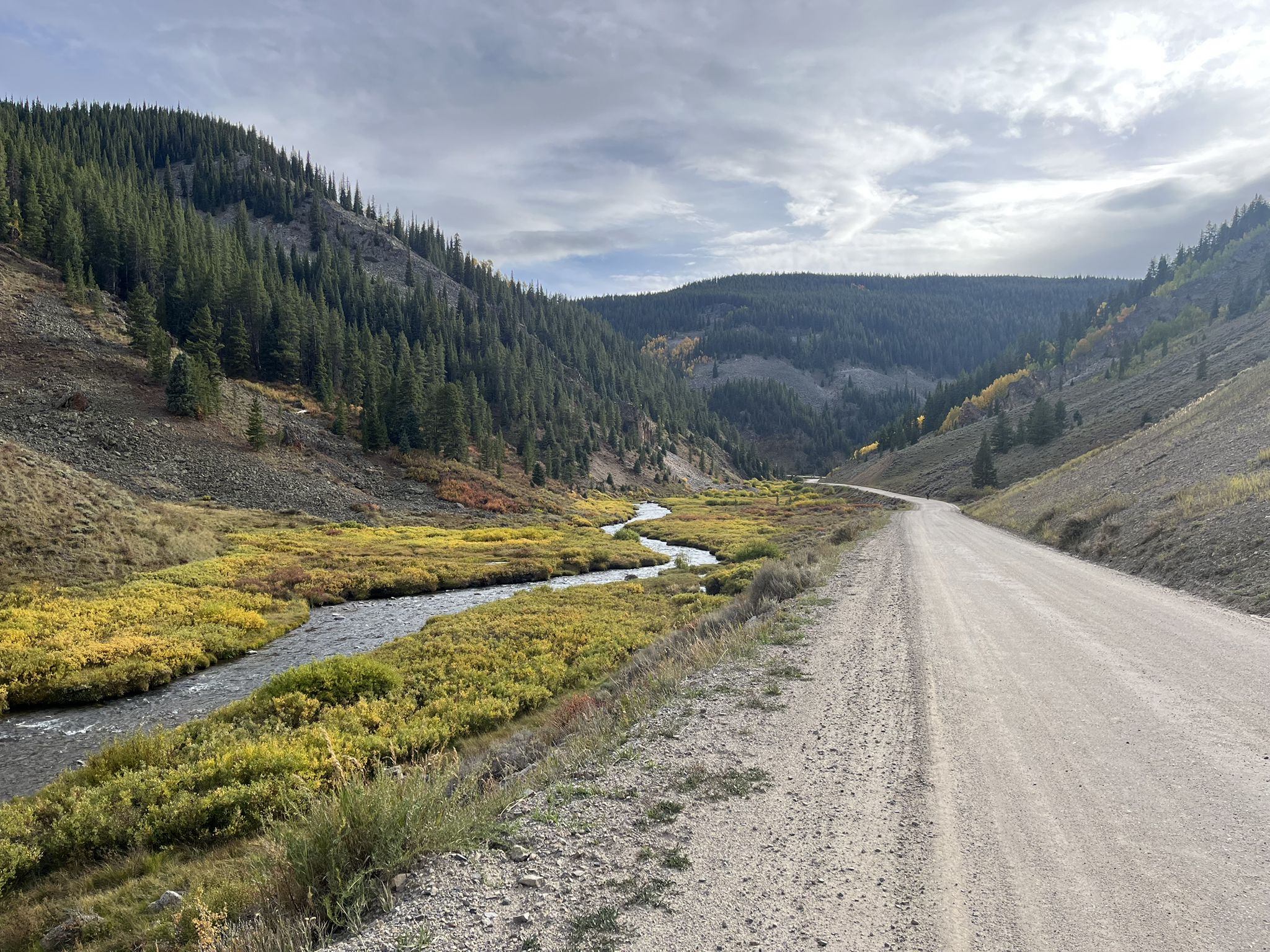 Dirt road alongside a winding river in a mountain valley under cloudy skies. - Doctor Park Loop