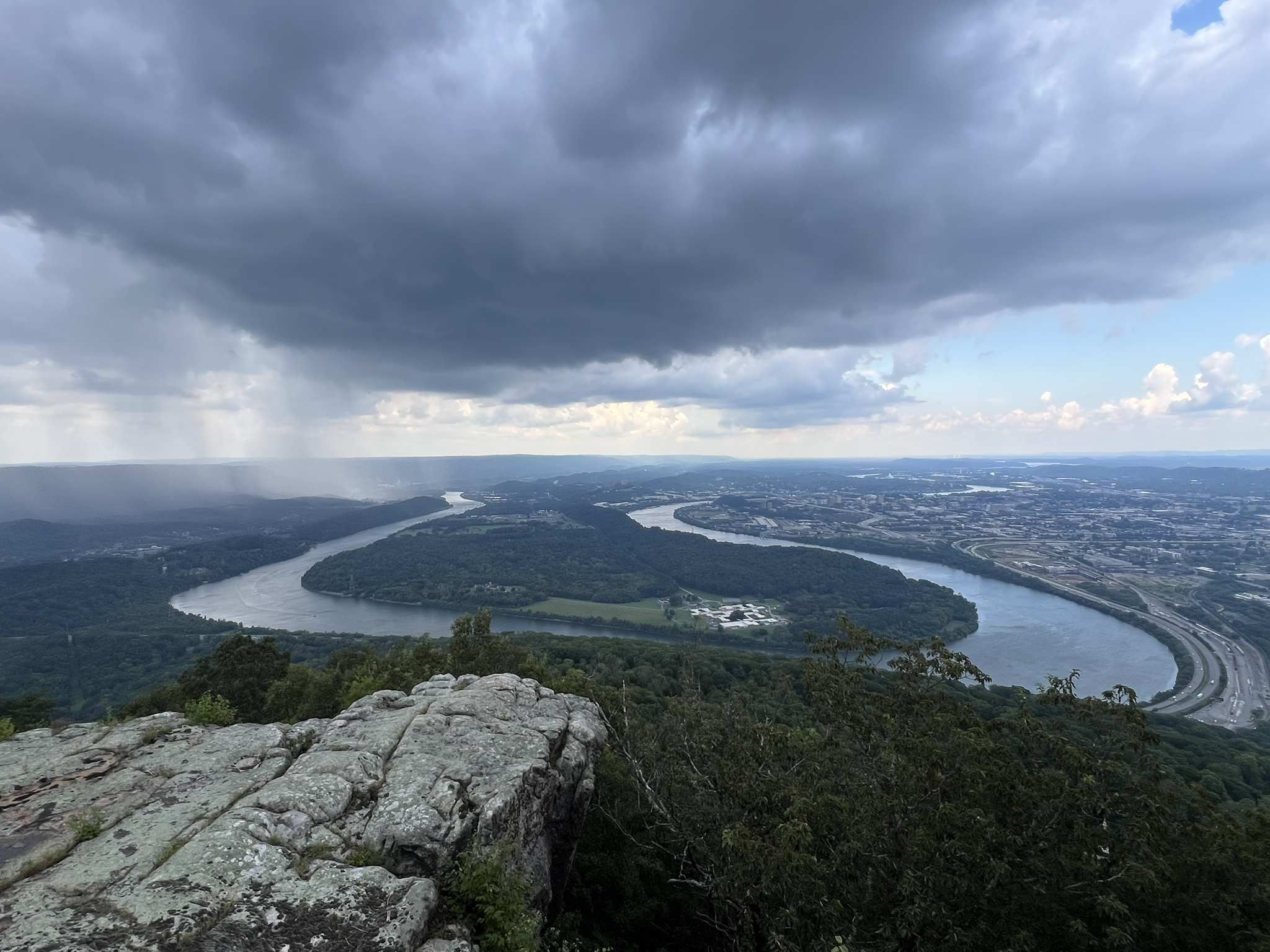 Panoramic view of a winding river and distant city under a stormy sky. - Bluff Trail