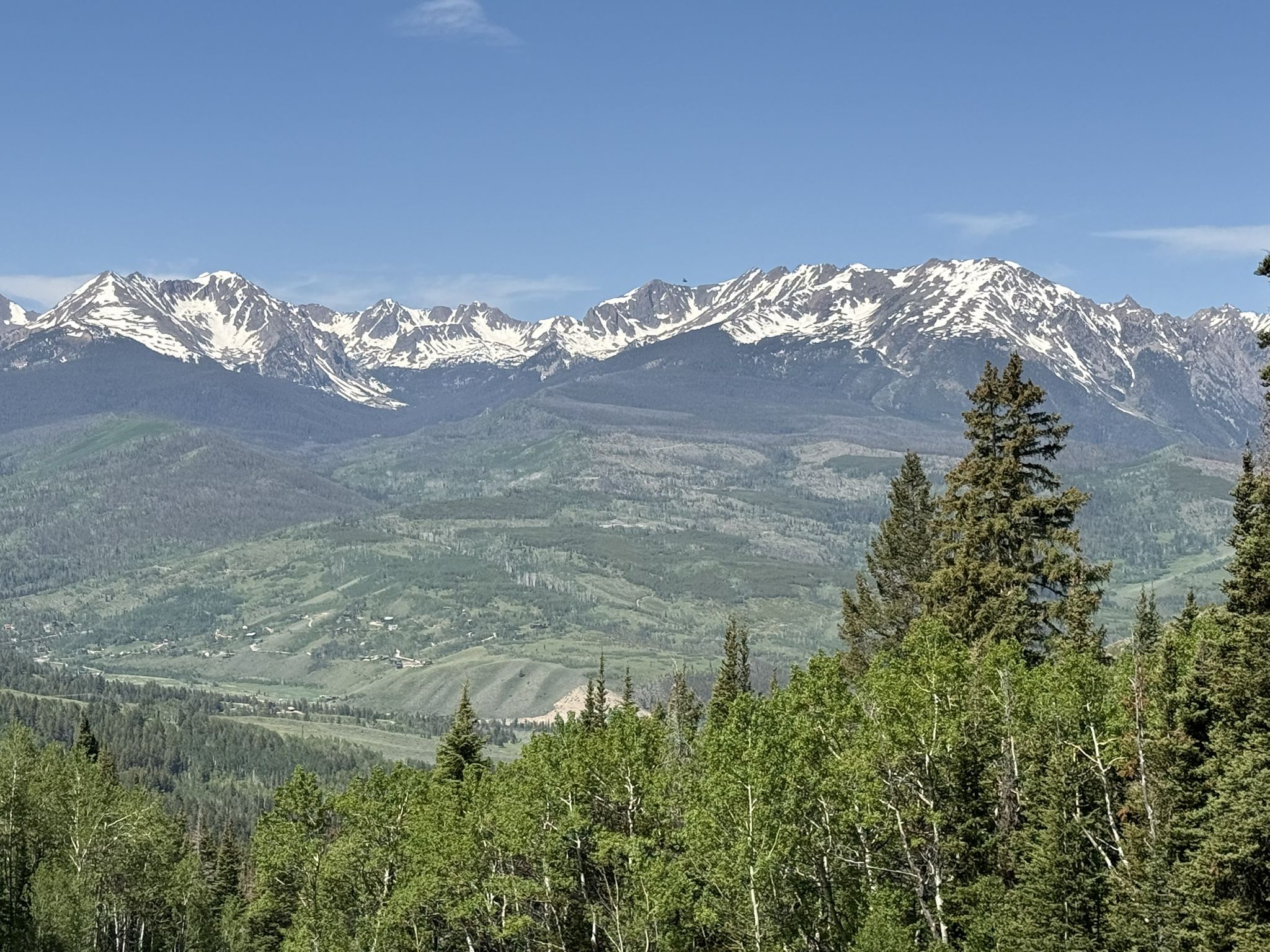 Snow-capped mountains overlook a green valley and forested hills on a clear day. - Ute Peak via Acorn Creek Trail