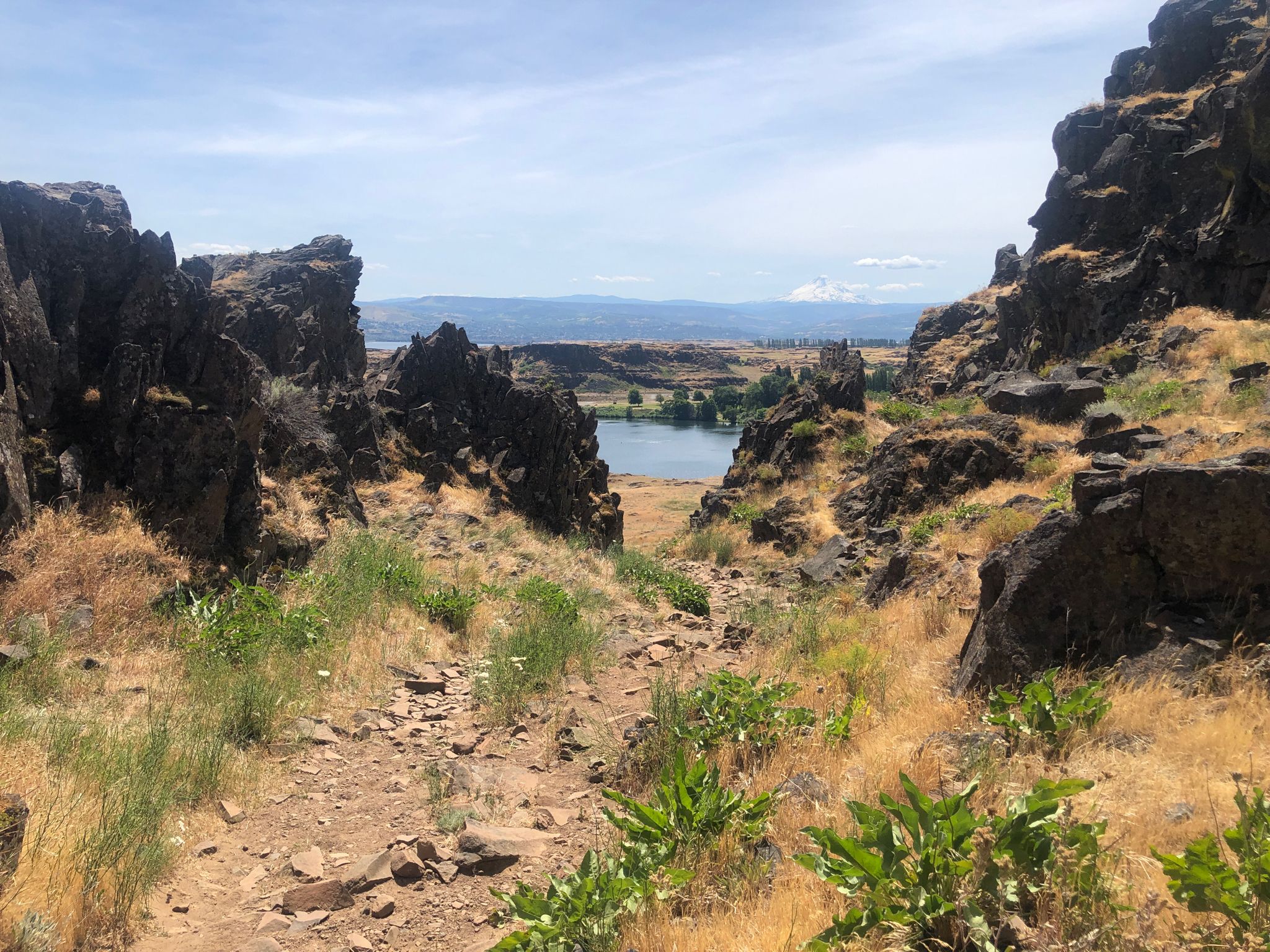 Rocky path descends through cliffs to a distant lake under a bright sky. - Horsethief Butte Trail