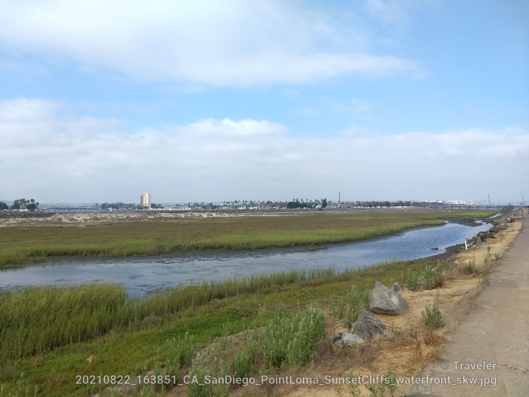 Overcast view of a marsh with a water channel and a dirt path. - Ocean Beach – San Diego River Bikeway loop from Amaya Drive