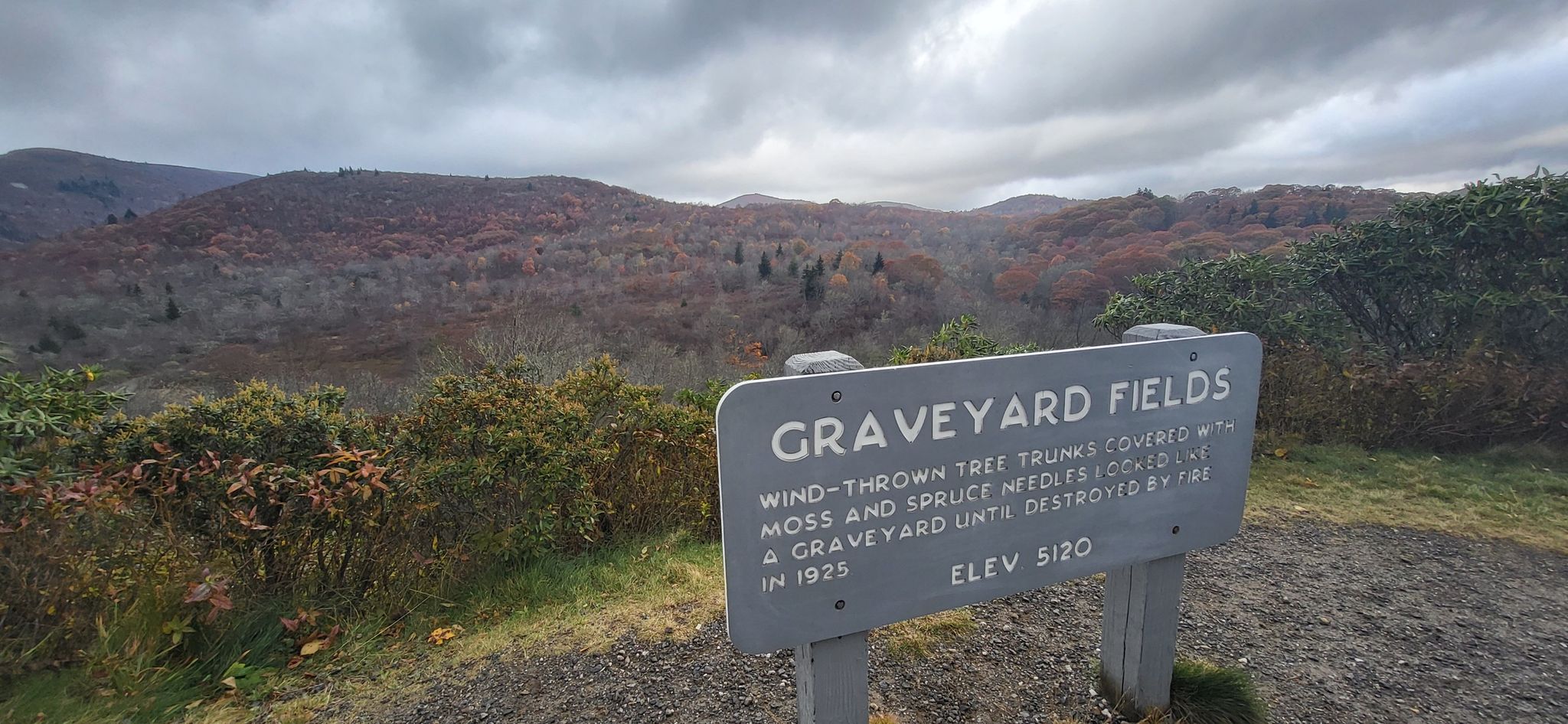 Wooden sign in a hilly landscape with muted autumn trees under cloudy sky. - Mountains to Sea Bicycle Route