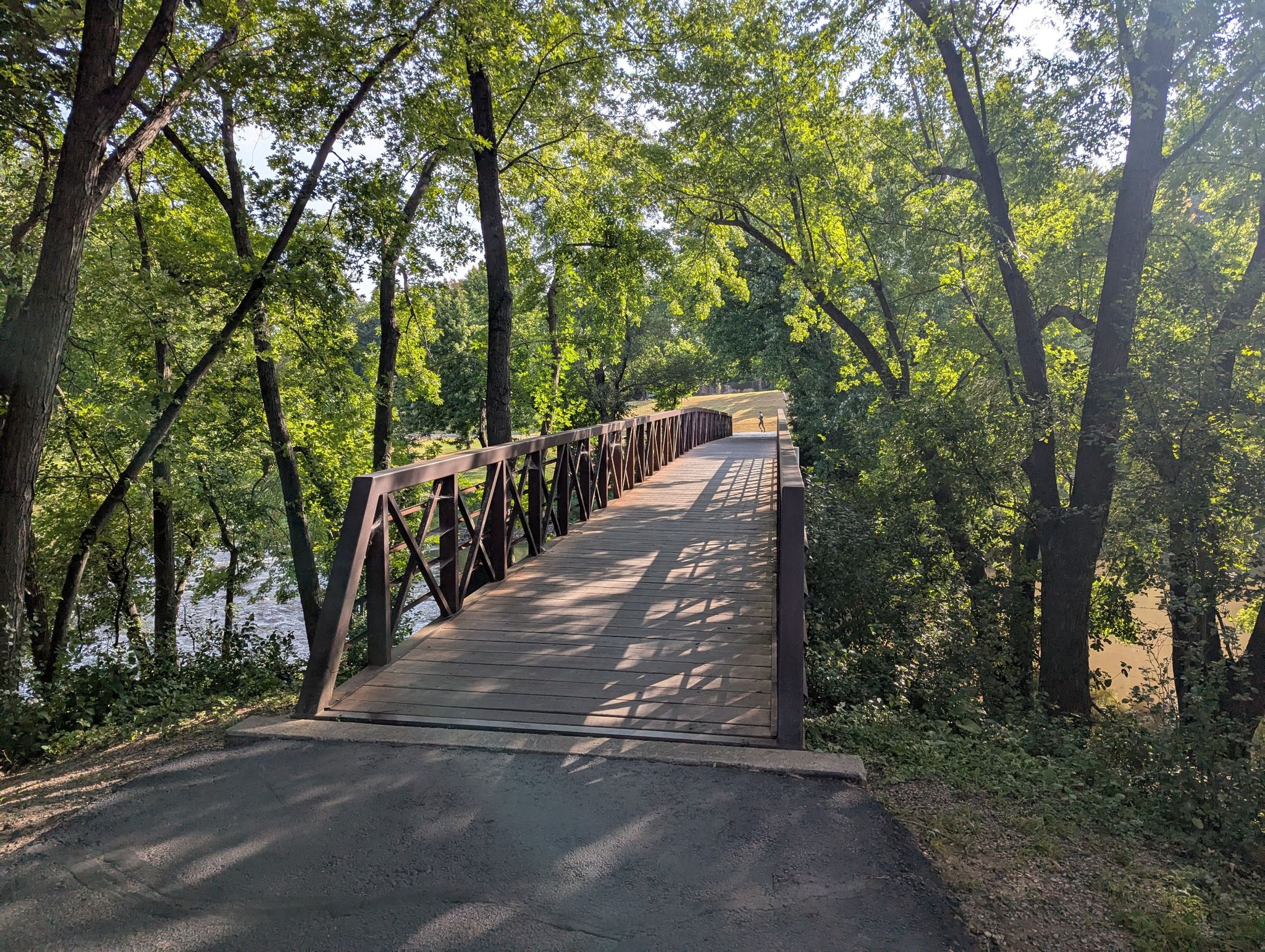 Wooden pedestrian bridge through a dense forest with dappled sunlight. - Running loop from Southern Hills Addition