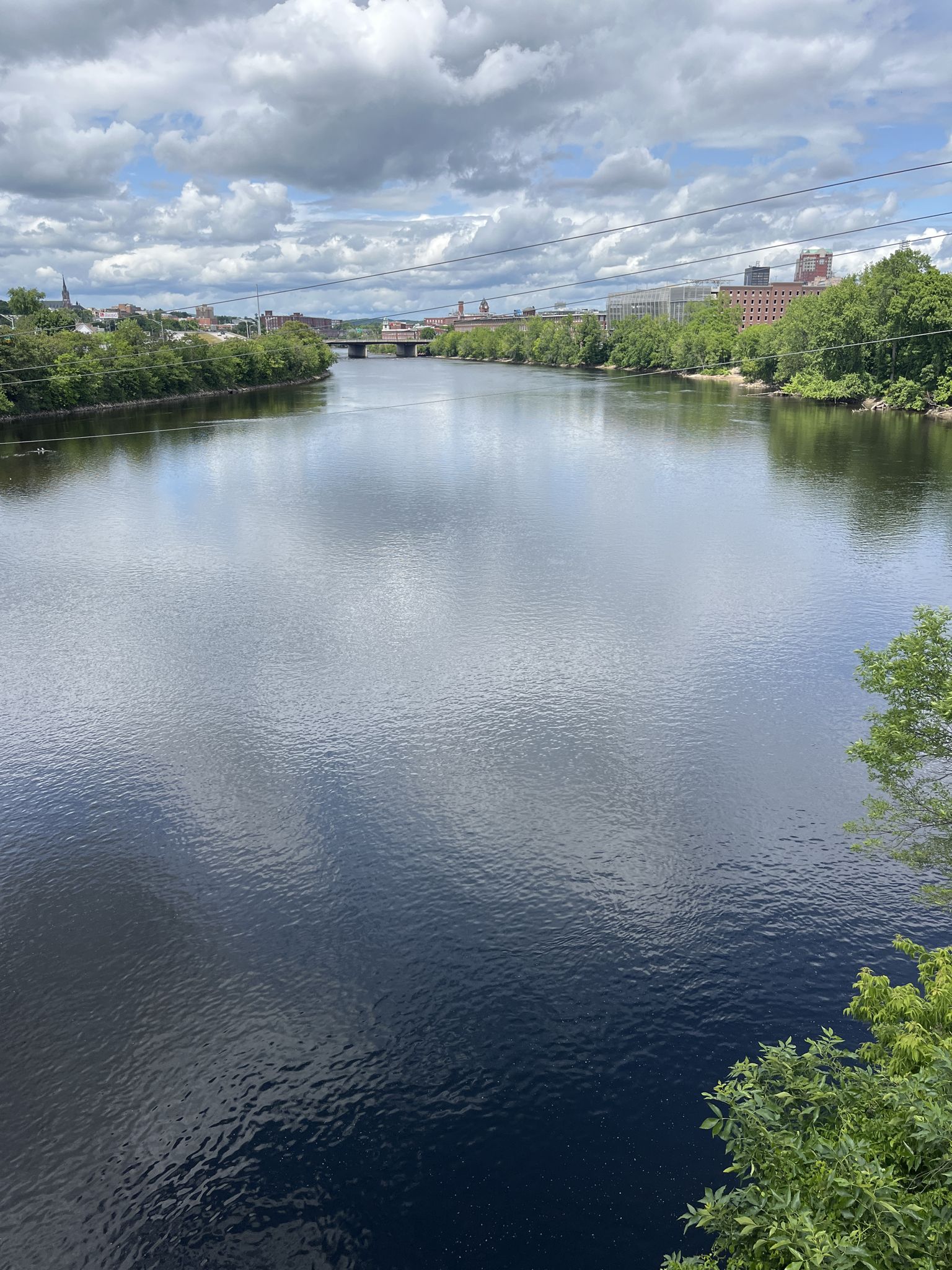 Wide river flowing through an urban landscape under a bright, cloudy sky. - Heritage and Piscataquog Trail