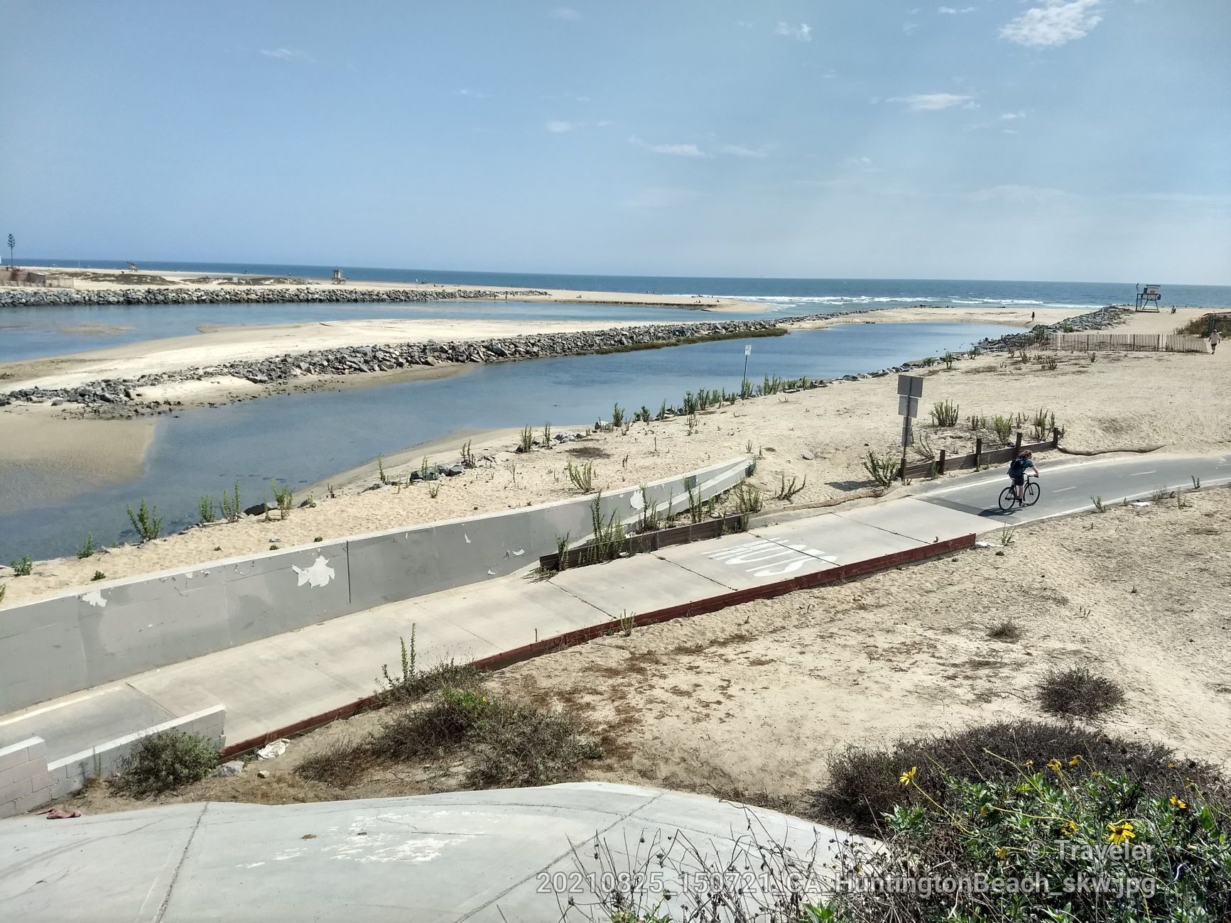 Cyclist on a paved path next to a water channel and sandy beach. - Santa Ana River Trail