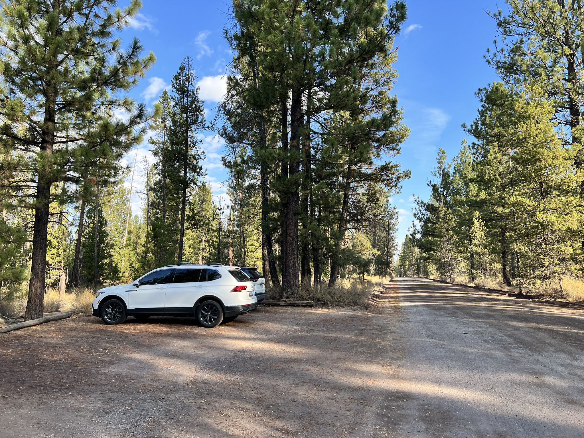A white SUV is parked on a dirt pull-off next to a forest road. - Lava Benham Trail – Sun Lava Trailhead loop from Sunriver Aquatics