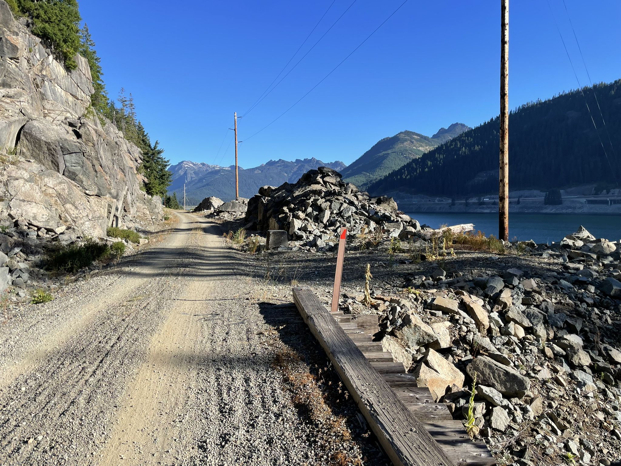 Gravel road beside a rocky cliff and lake, with distant mountains under clear sky. - Keechelus Lake – "The Seals" loop from Snoqualmie Pass