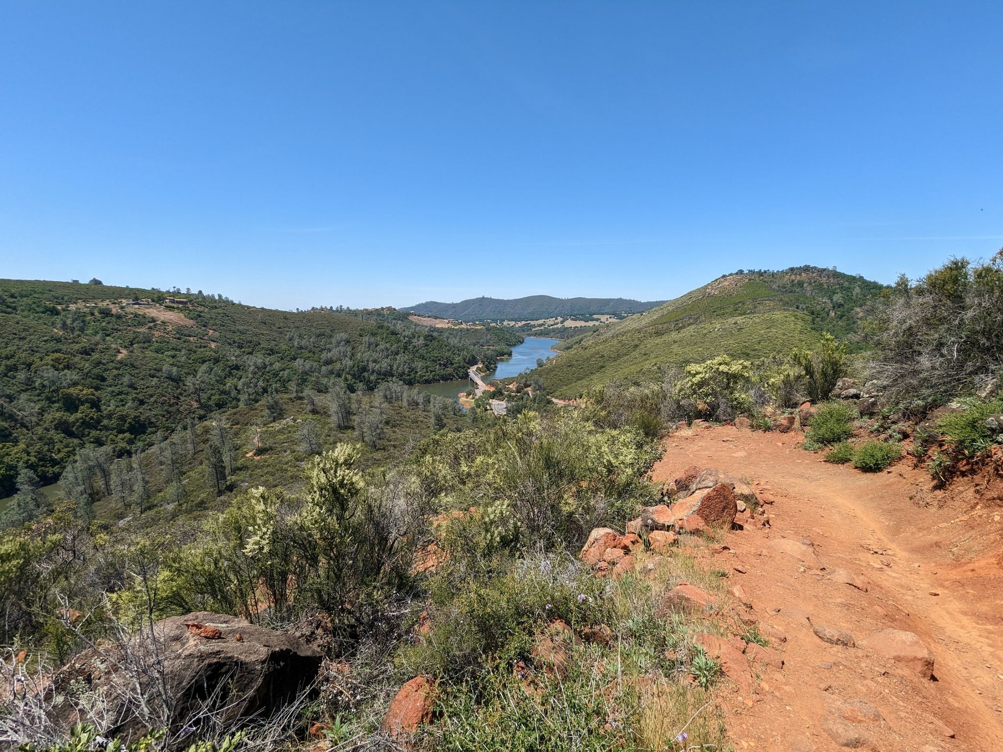 Sunny view of a winding river through green, brush-covered hills from a dirt path. - South Fork American River Trail