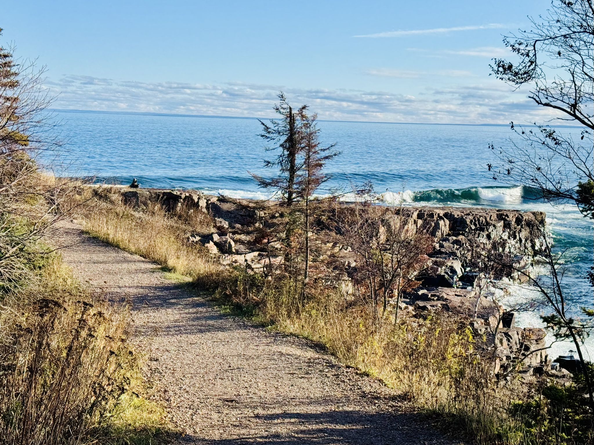 Dirt path leading to a rocky coastline with ocean waves under a blue sky. - Two Harbors Lighthouse