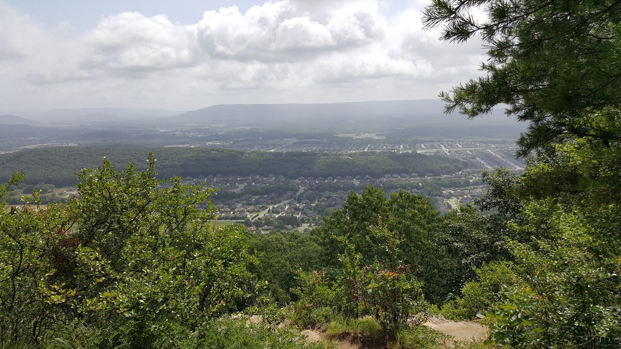 Scenic overlook of green trees, distant town, and rolling hills under clouds. - Bill and Marion Certain Trail