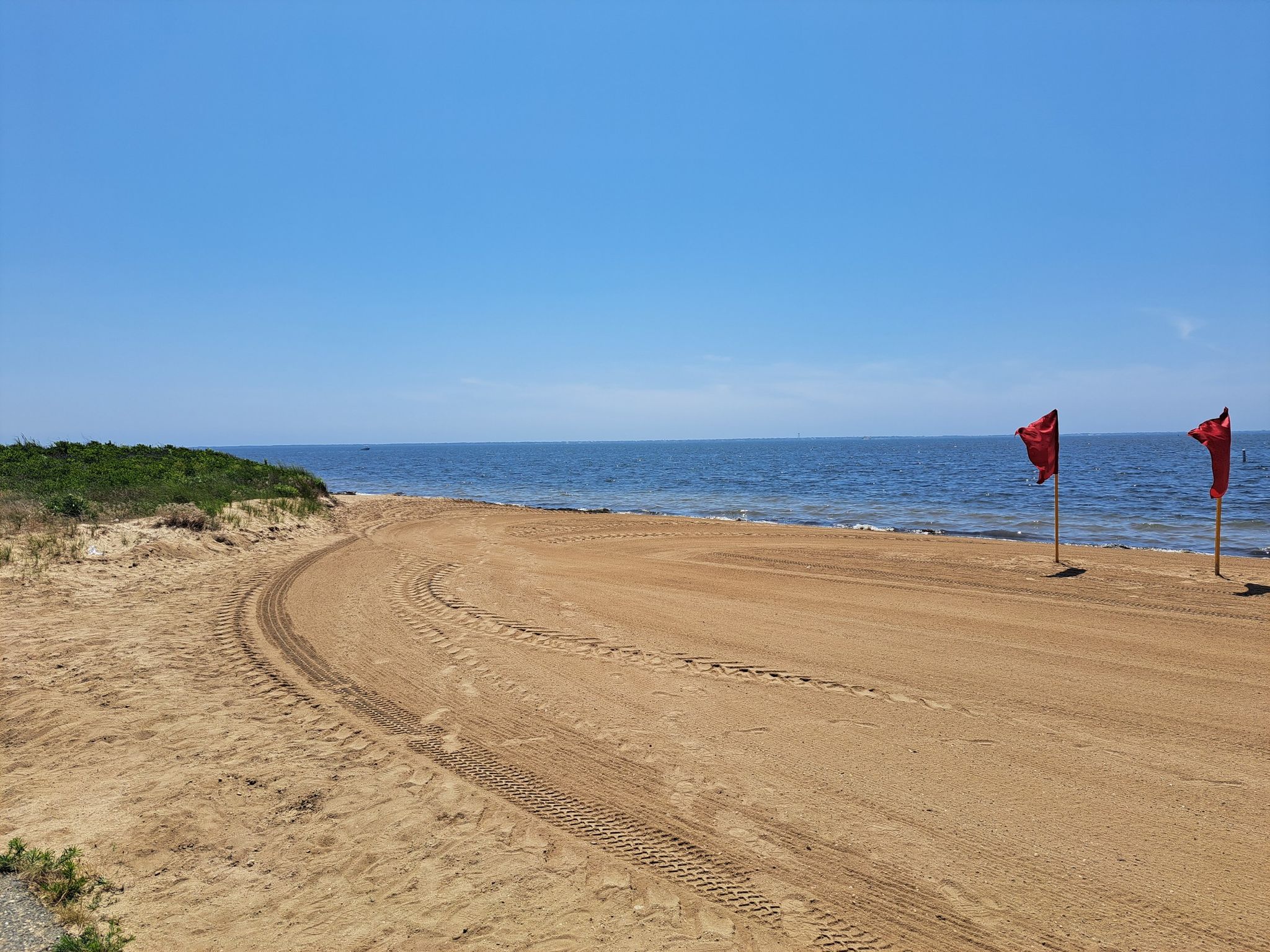 Sunny beach with tire tracks, blue ocean, and two red flags. - West Beach – Overlook Beach loop from Great River