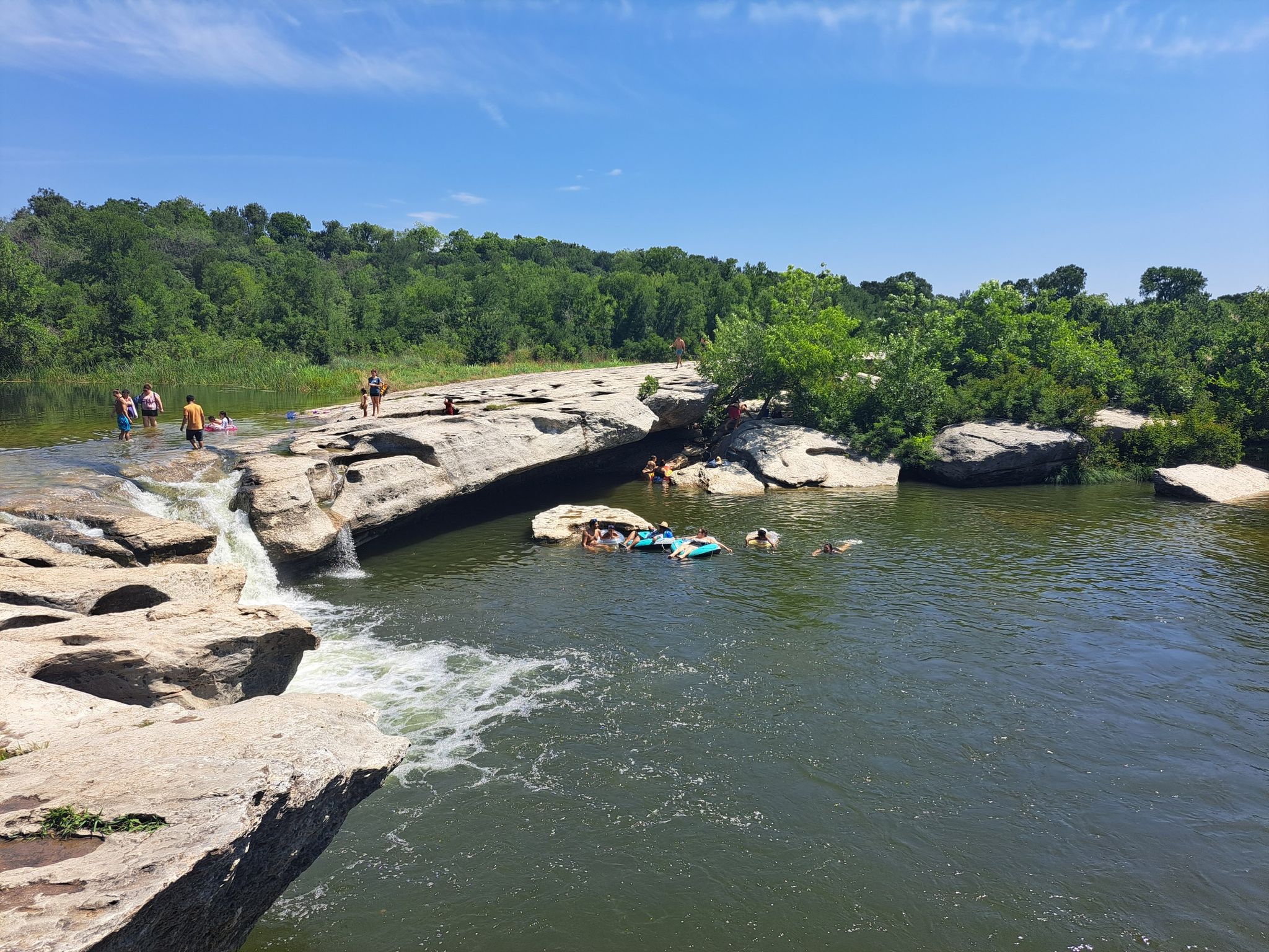 Many people swimming and floating in a river with small waterfalls. - Onion Creek Hike and Bike Trail