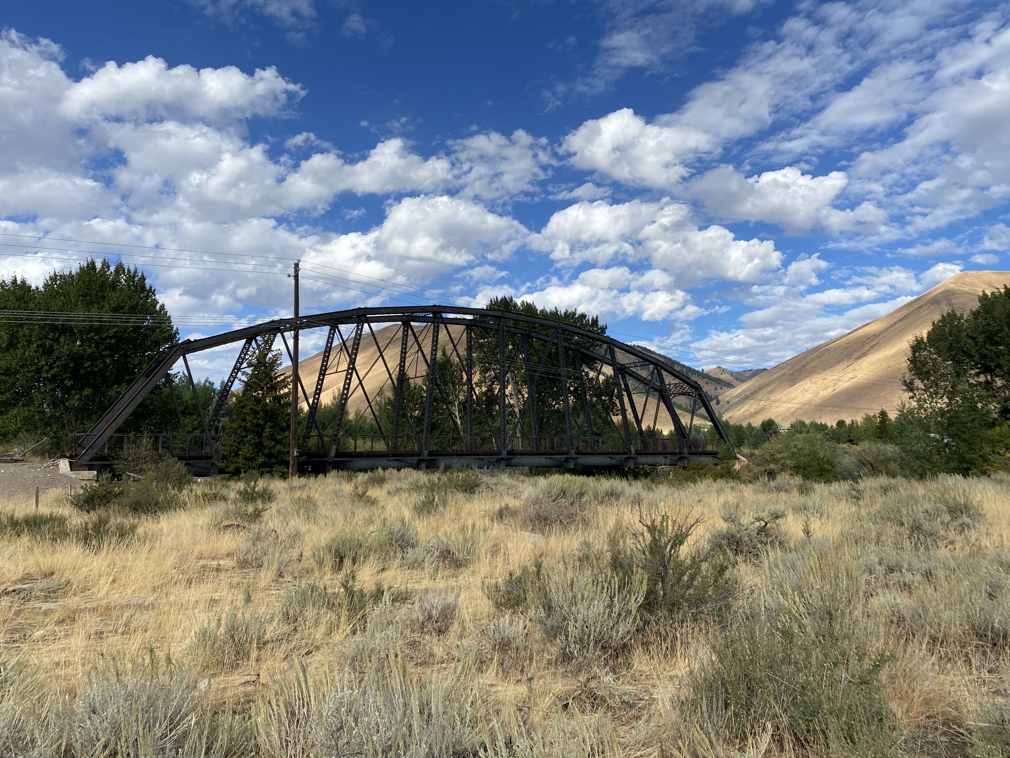 Old black metal truss bridge surrounded by dry brush under a bright blue sky. - Penny Mountain – Big Wood River loop from Sun Valley