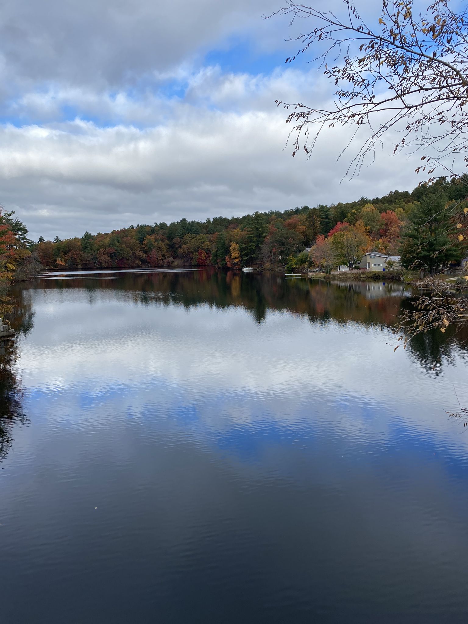 Lake reflecting cloudy sky, surrounded by autumn trees and distant houses. - Goffstown Rail Trail