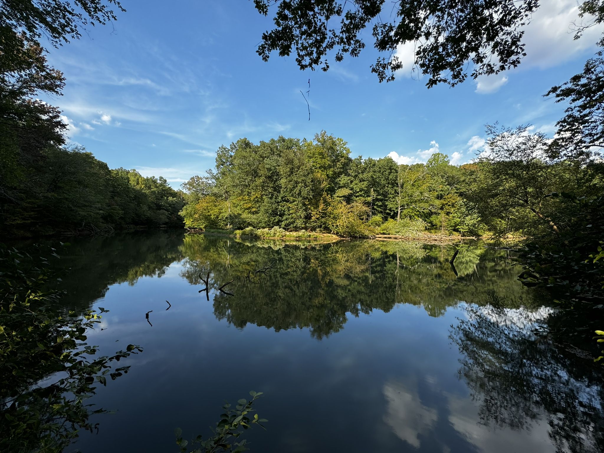Calm lake reflects blue sky and lush green forest on its banks. - New Manchester Mill Ruins loop from Jack's Hill