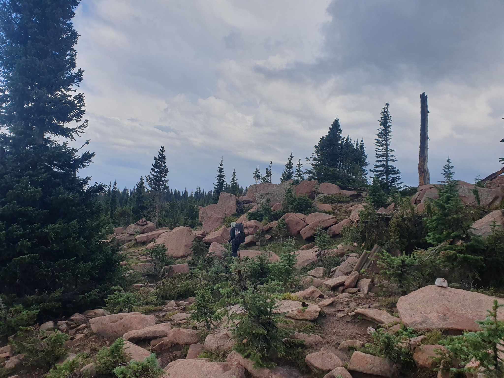 A person hikes uphill through a rocky, forested landscape under an overcast sky. - Green Mountain and Continental Divide Trail Loop