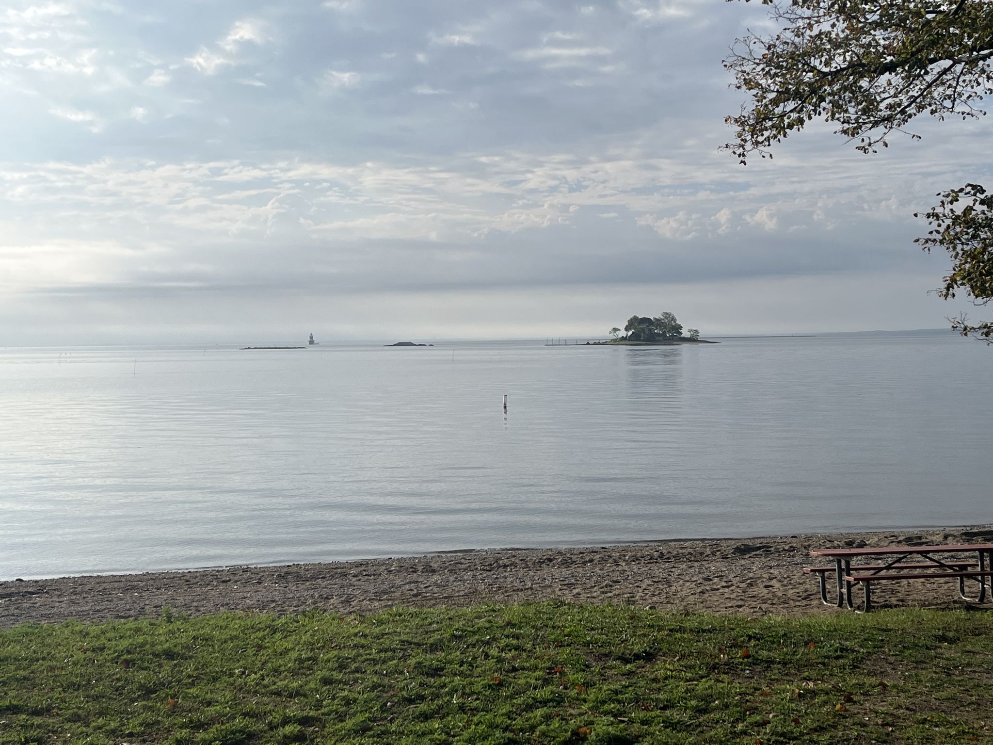Overcast view of a calm lake with a distant island and a picnic table. - Calf Pasture Beach