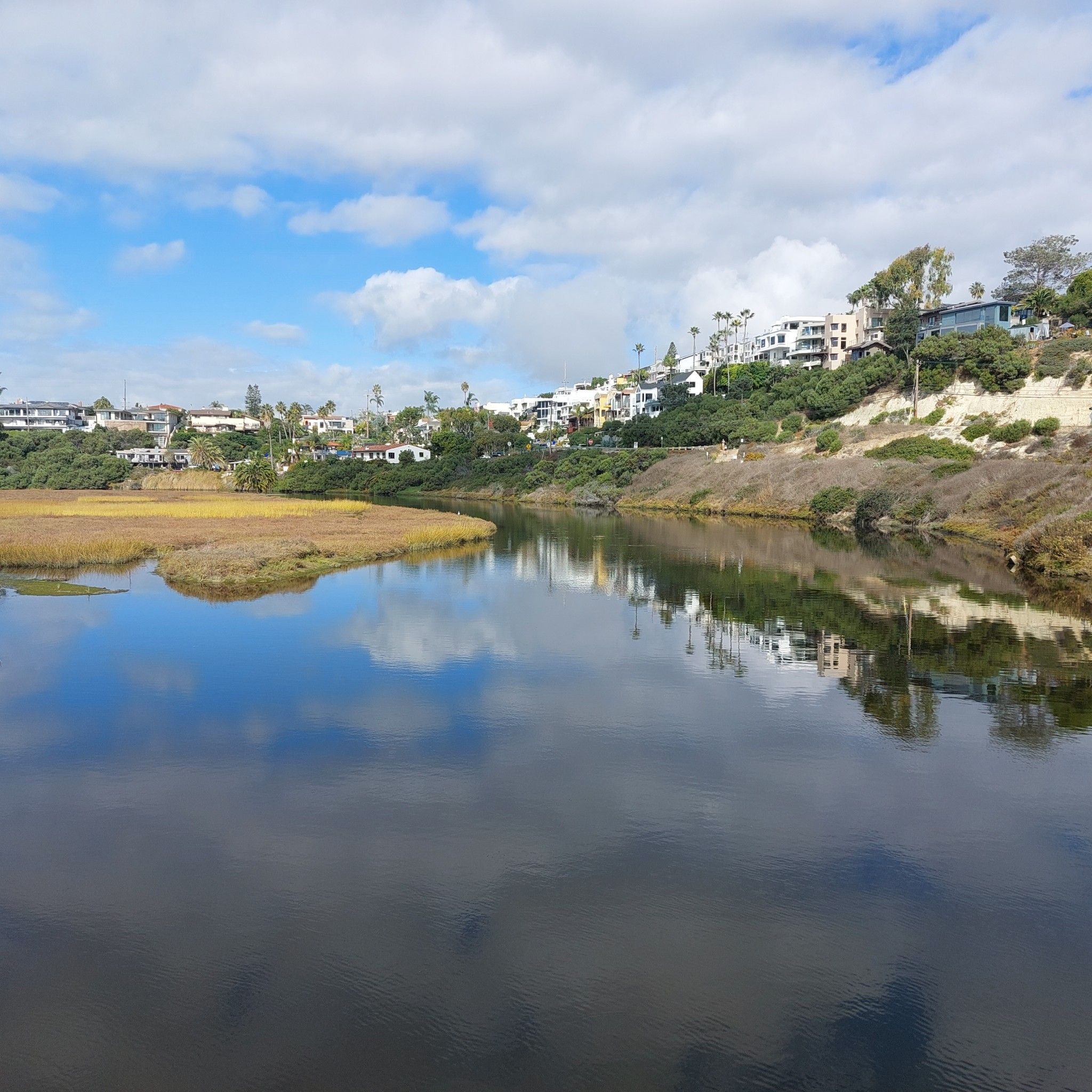 Calm estuary reflecting sky and houses on a hill, cloudy day. - Pelican Island loop from Solana Beach