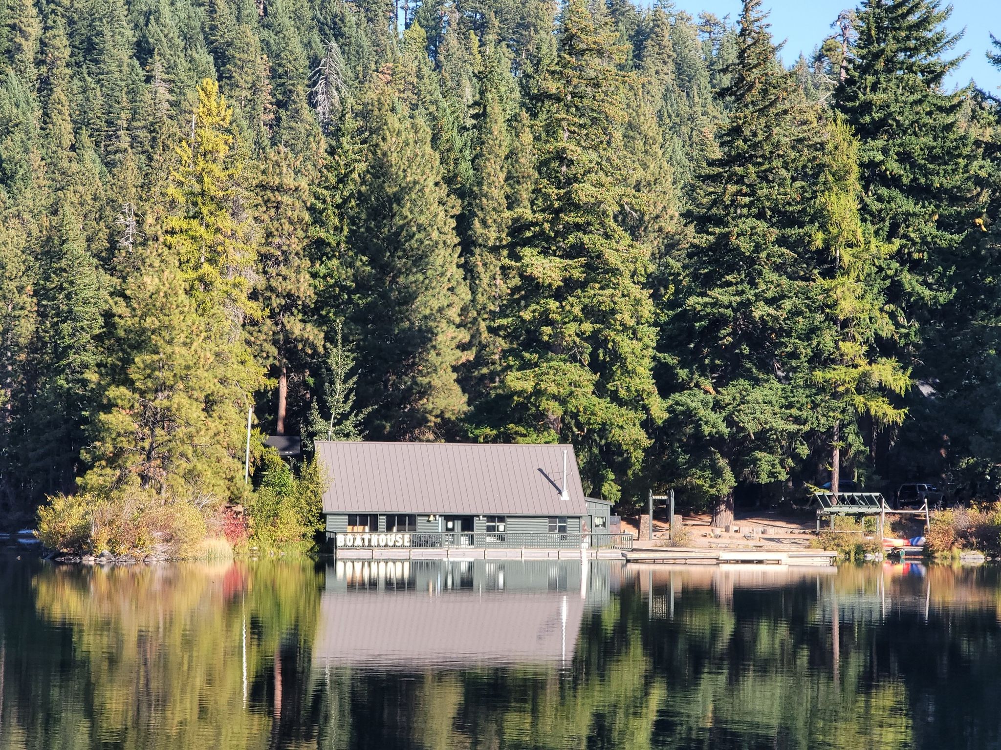 Boathouse on a calm lake, surrounded by dense green forest under bright light. - Suttle Lake Loop Trail