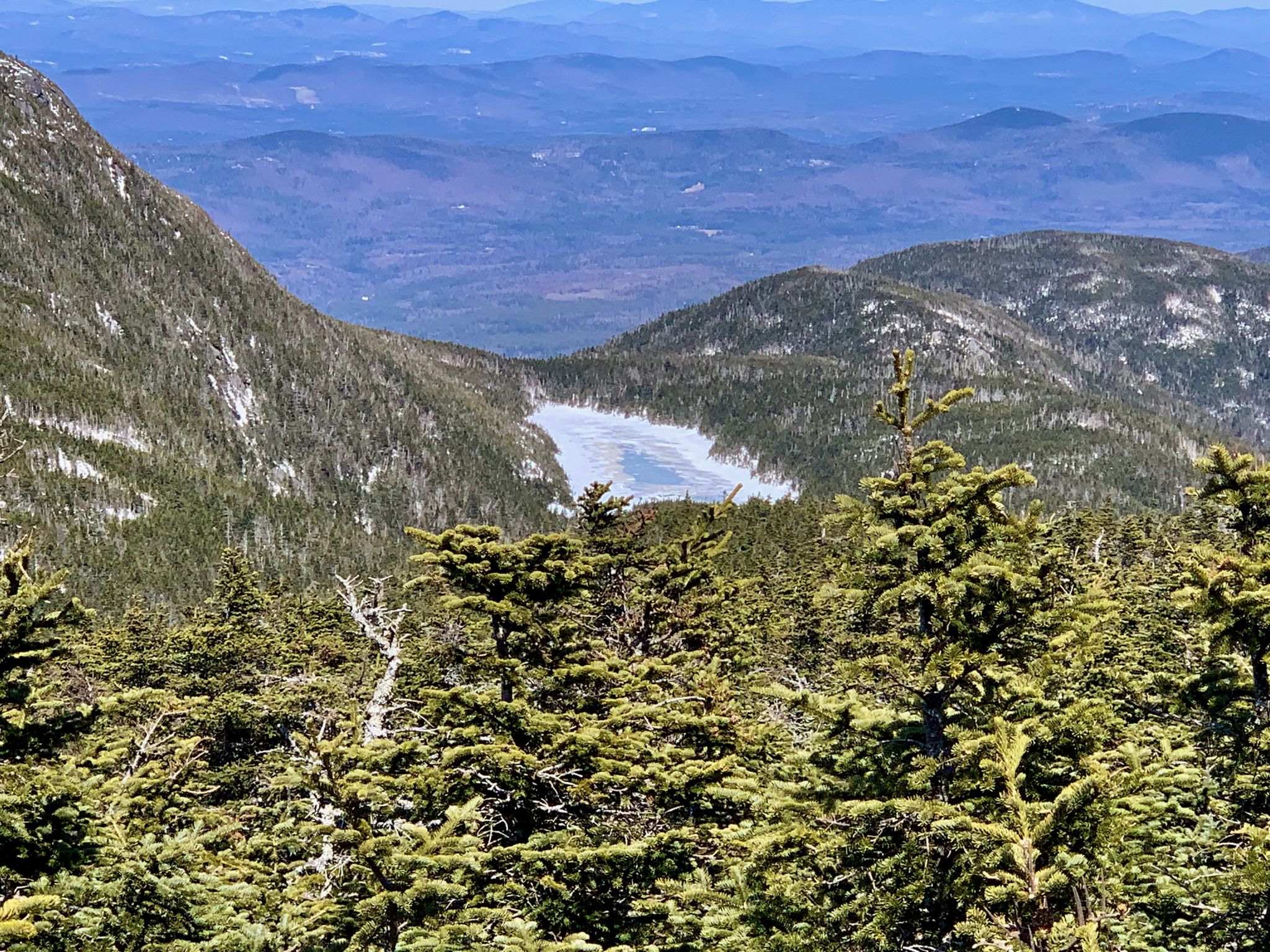 Partially frozen lake surrounded by snow-dusted mountains and evergreen trees. - North Peak – South Peak Kinsman Mountain loop from Ham Branch