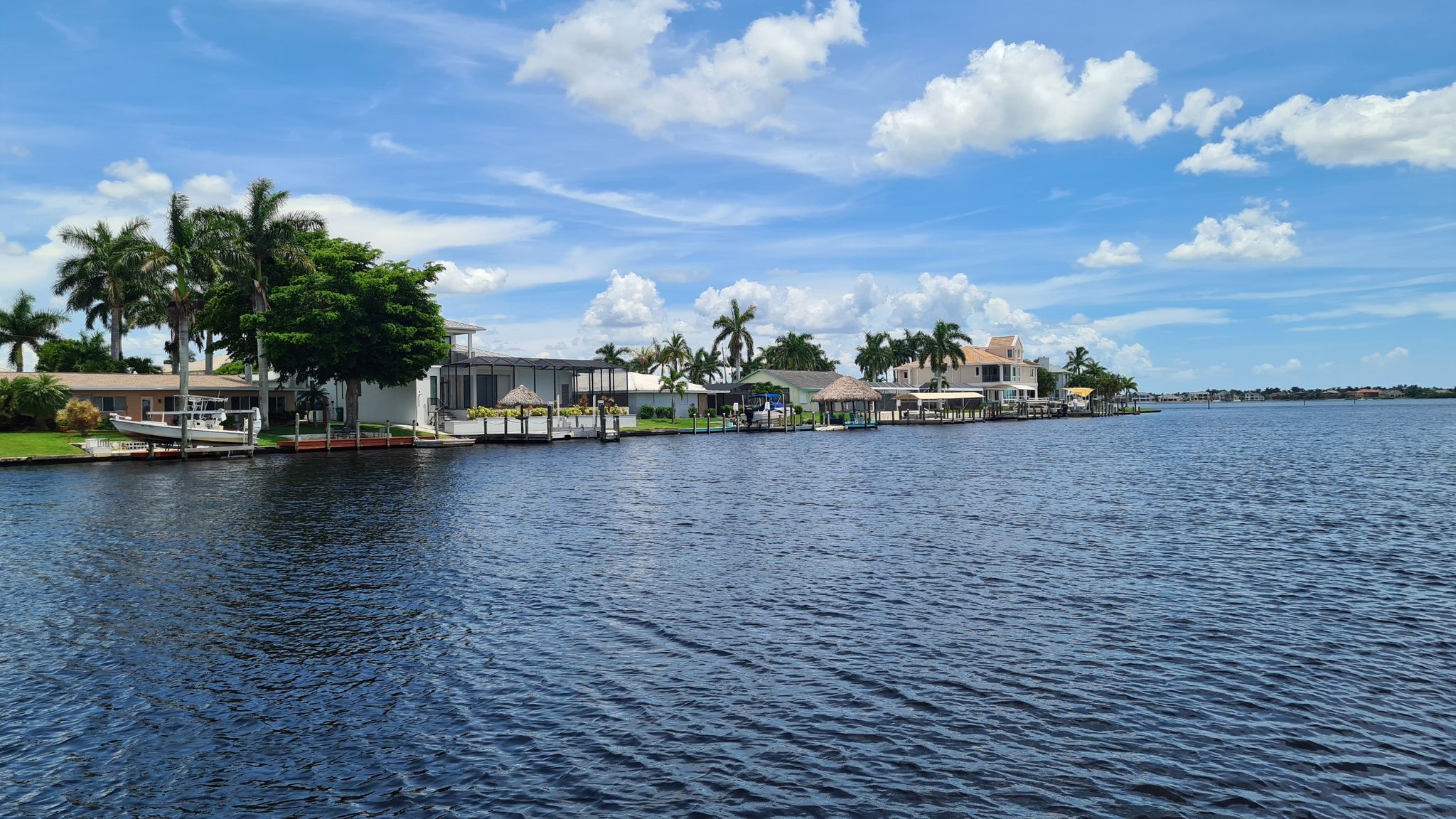 Waterfront houses and palm trees line a calm canal under a bright sky. - Cape Coral loop