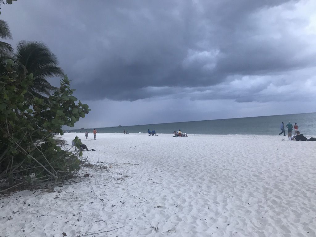 People on a wide sandy beach under a dark, stormy sky. - Downtown Naples and Naples Beach loop