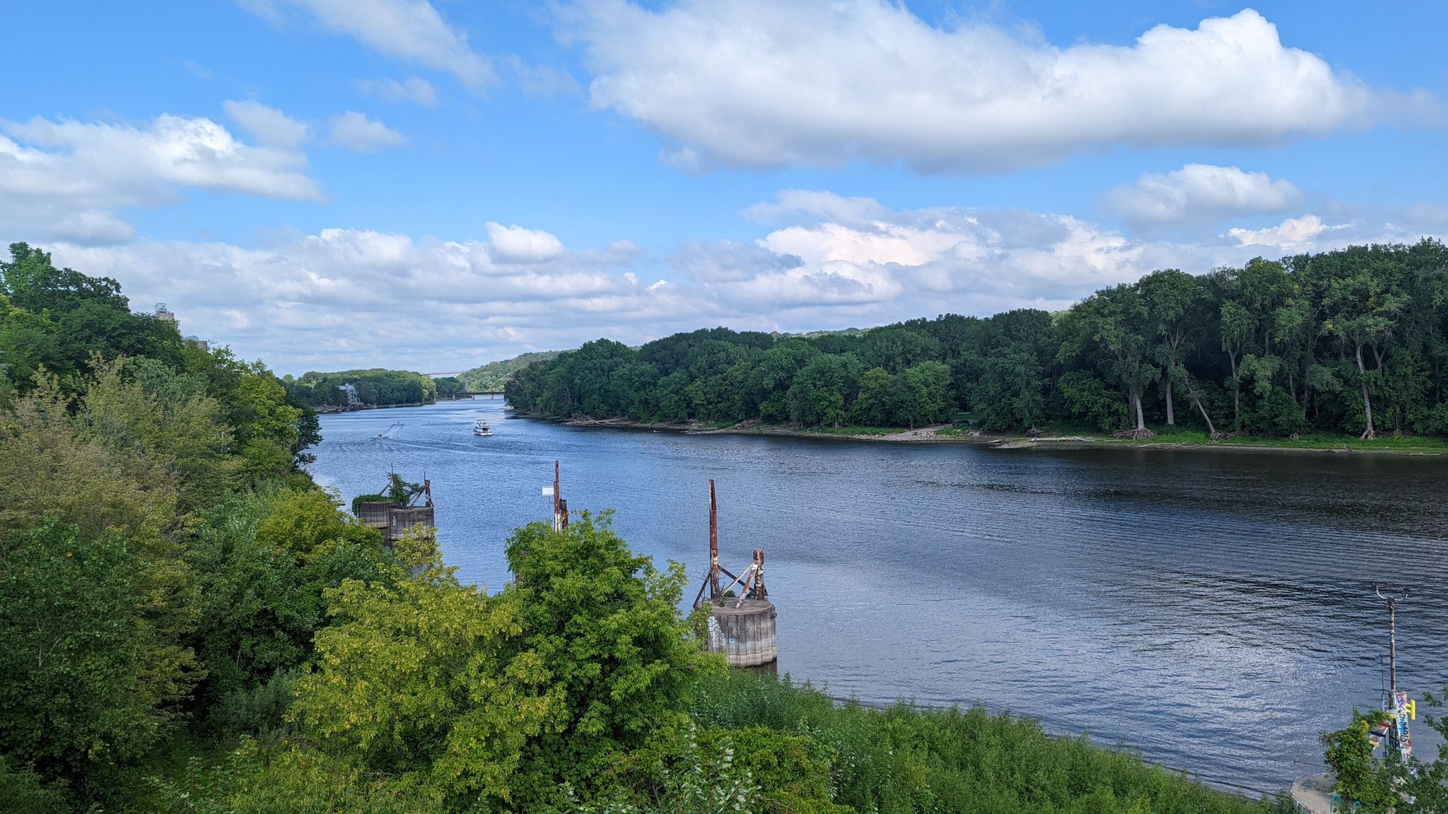 Wide river flowing through dense green forests under a partly cloudy sky. - Samuel H. Morgan Regional Trail