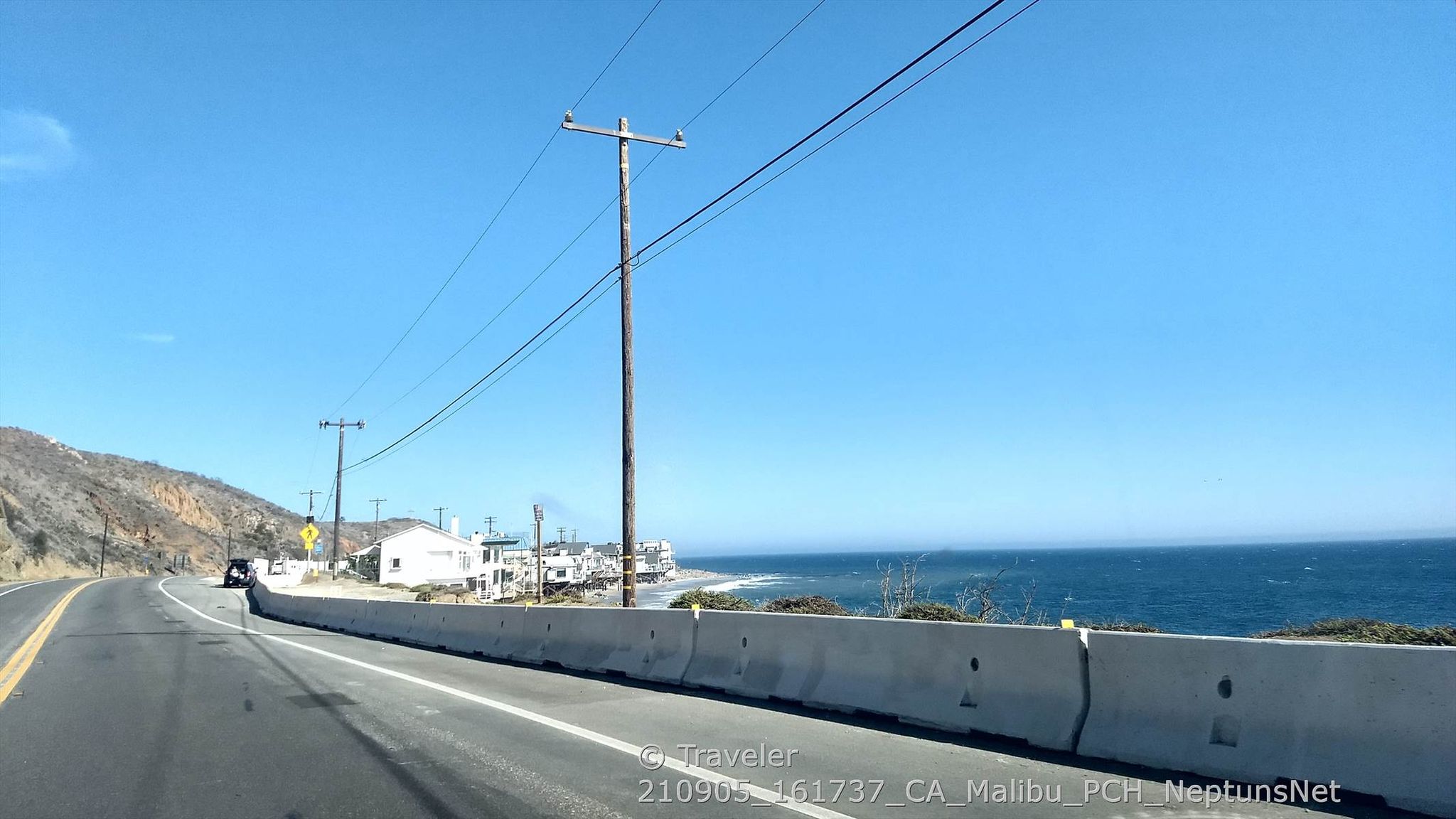 Coastal road with power lines, buildings, and ocean under a clear sky. - Neptune's Net loop from Old Malibu