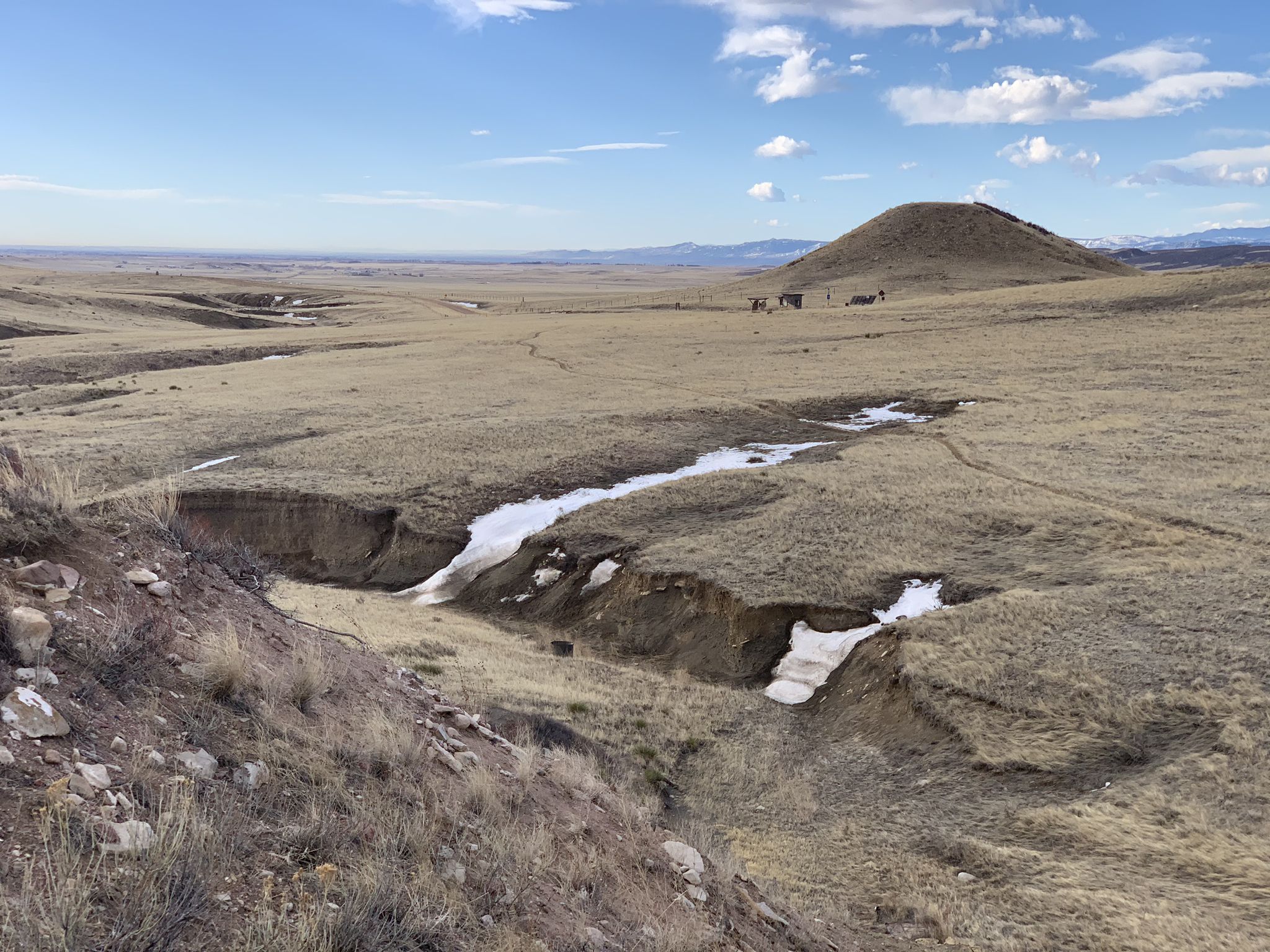 Expansive dry grassland with snow patches in a gully under a bright sky. - Pronghorn Loop
