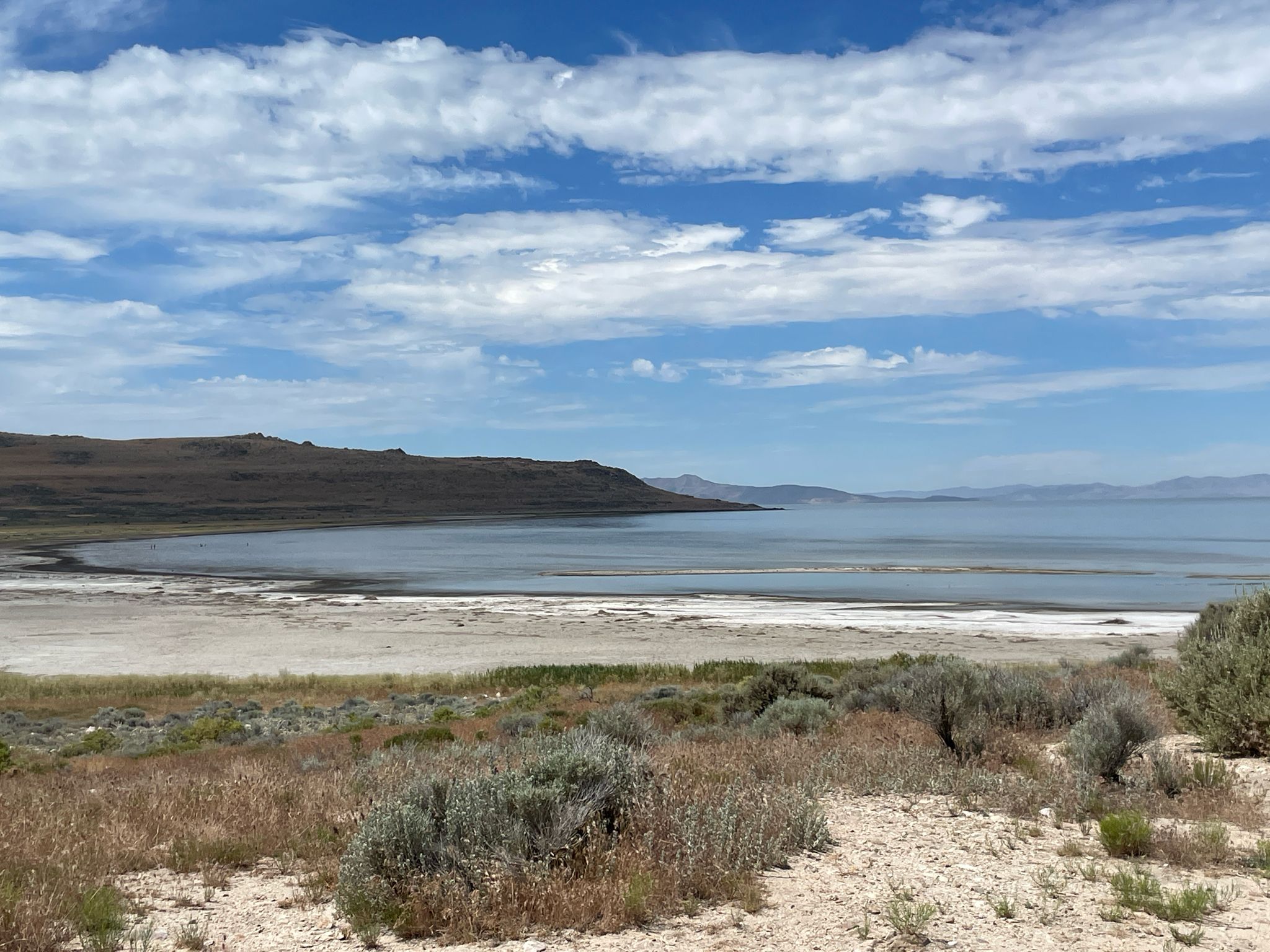 Calm bay with sandy shore, low hills, and a partly cloudy sky. - Ladyfinger Point – Antelope Island State Park loop from Syracuse