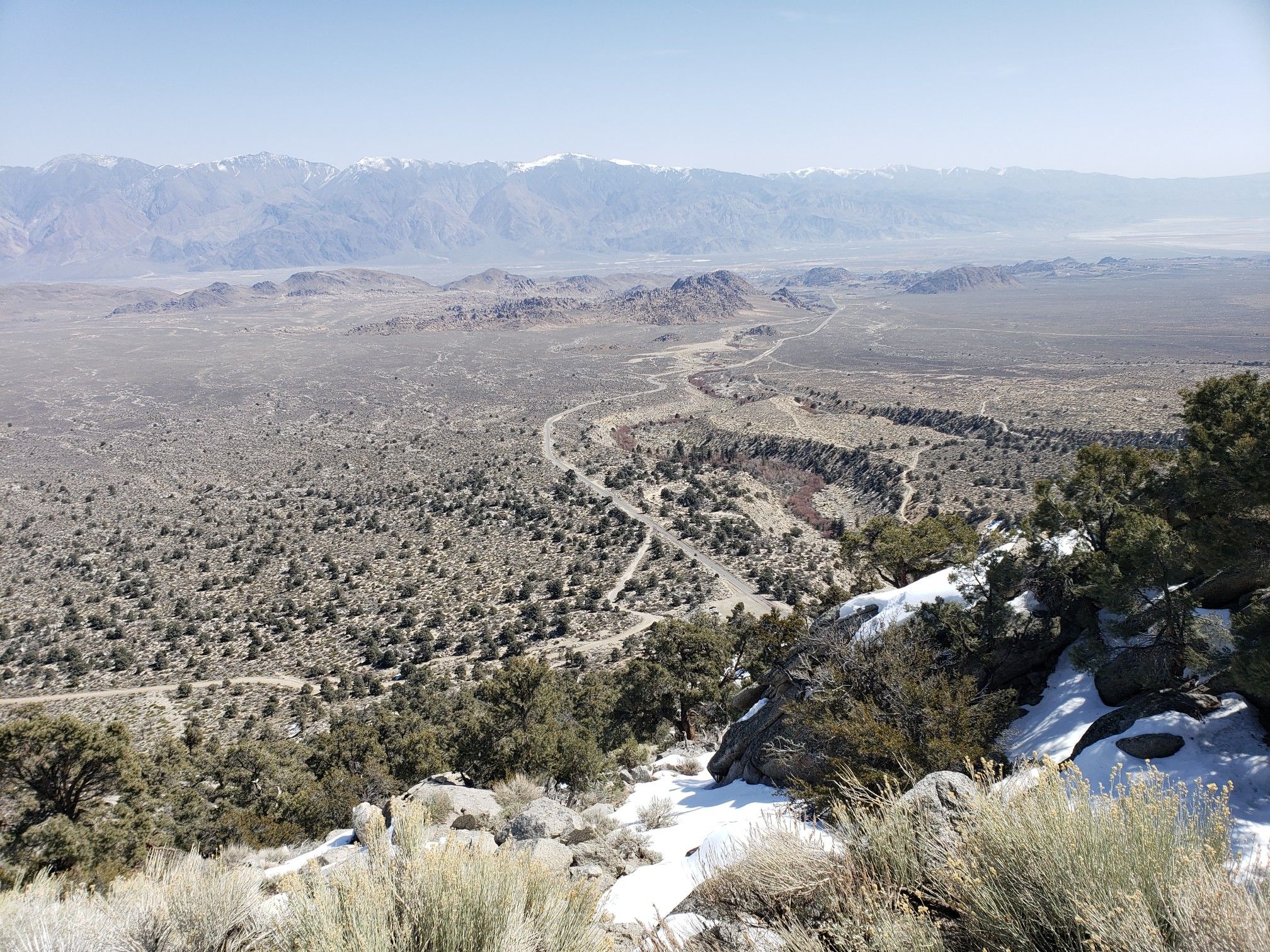 A high view of a vast arid valley with winding roads and distant mountains. - Whitney Portal Road