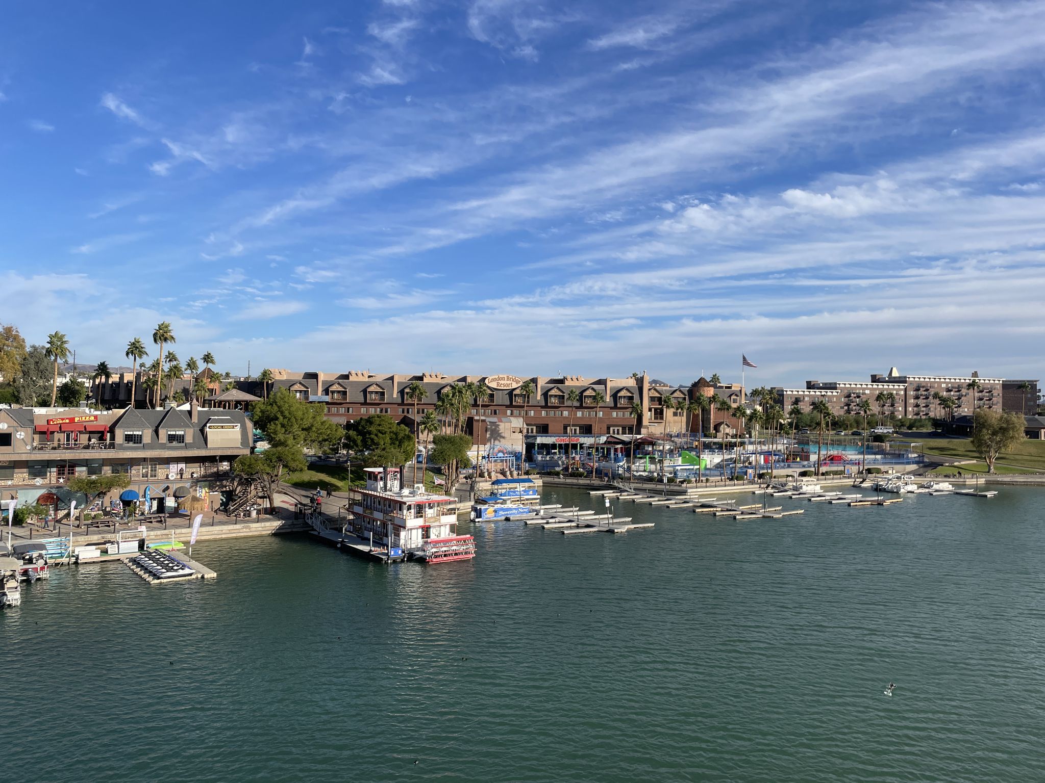 Waterfront buildings and boats docked in a marina under a bright, cloudy sky. - Lake Havasu City loop