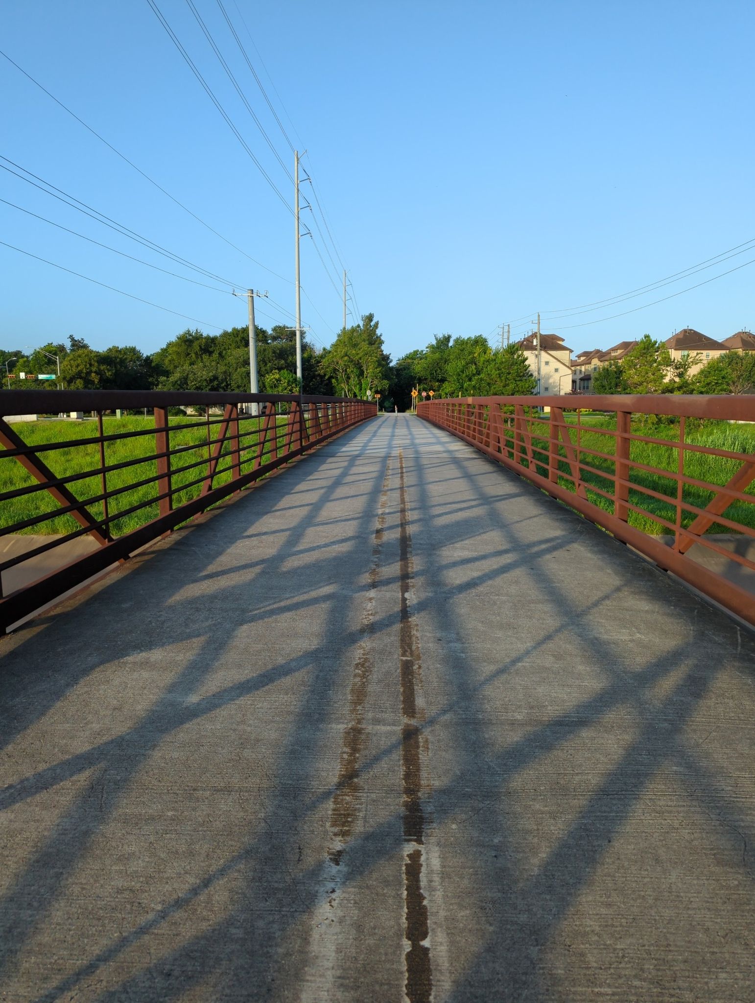 A long pedestrian bridge with red railings casts shadows on a sunny day. - The Cistern at Buffalo Bayou Park – Main Street Bridge loop from Northline Transit Center/HCC