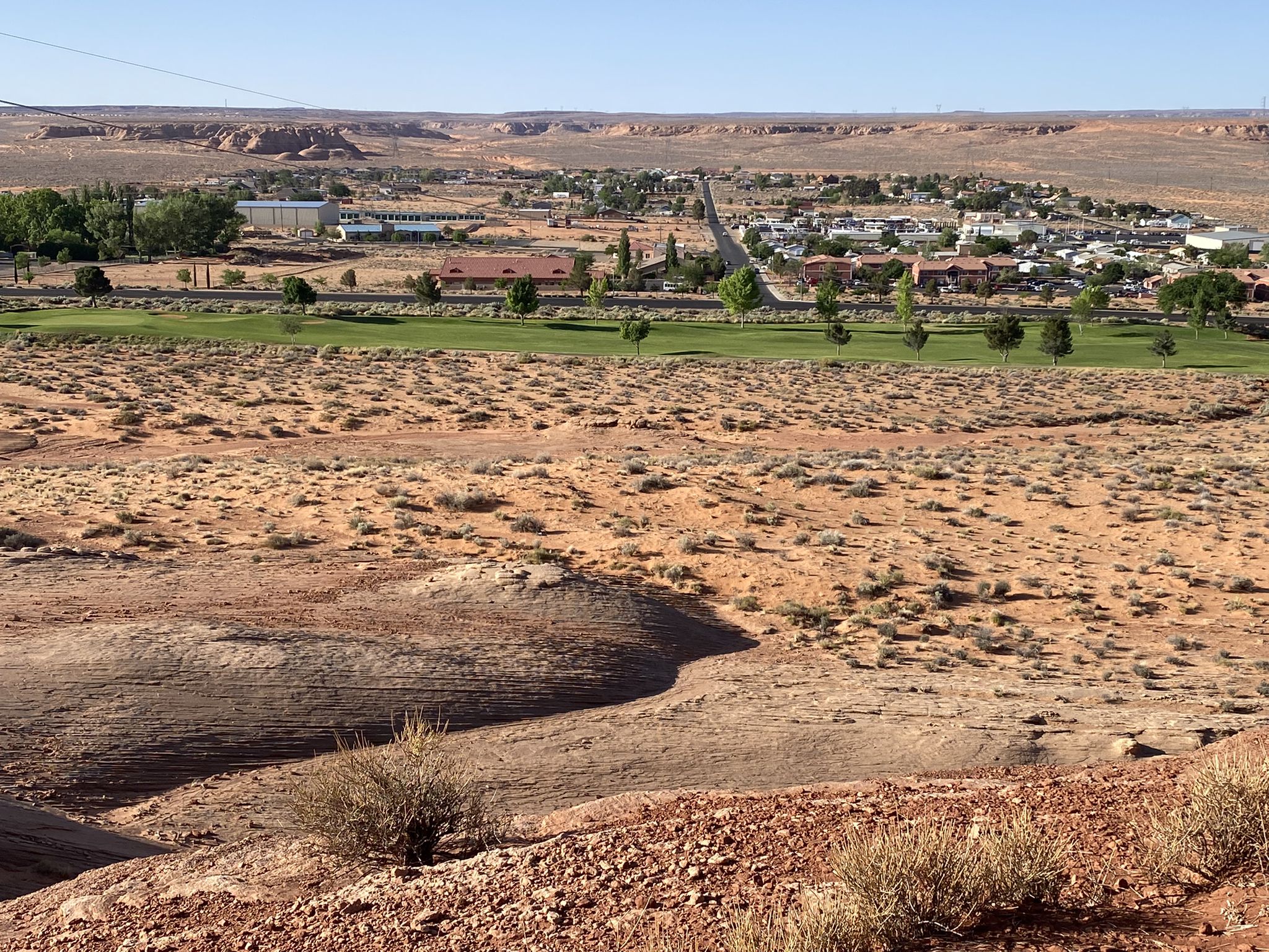 An arid foreground overlooks a green golf course and distant town. - Glen Canyon Dam Viewpoint – Glen Canyon Dam Overlook loop from Page