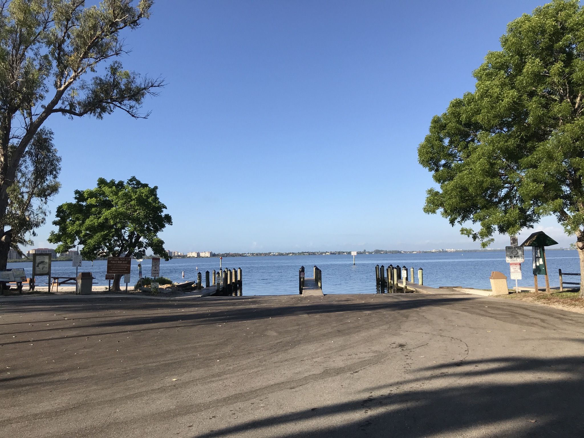 A paved boat access area leading to a wide body of water on a sunny day. - Yacht Club Community Park loop from Hooters