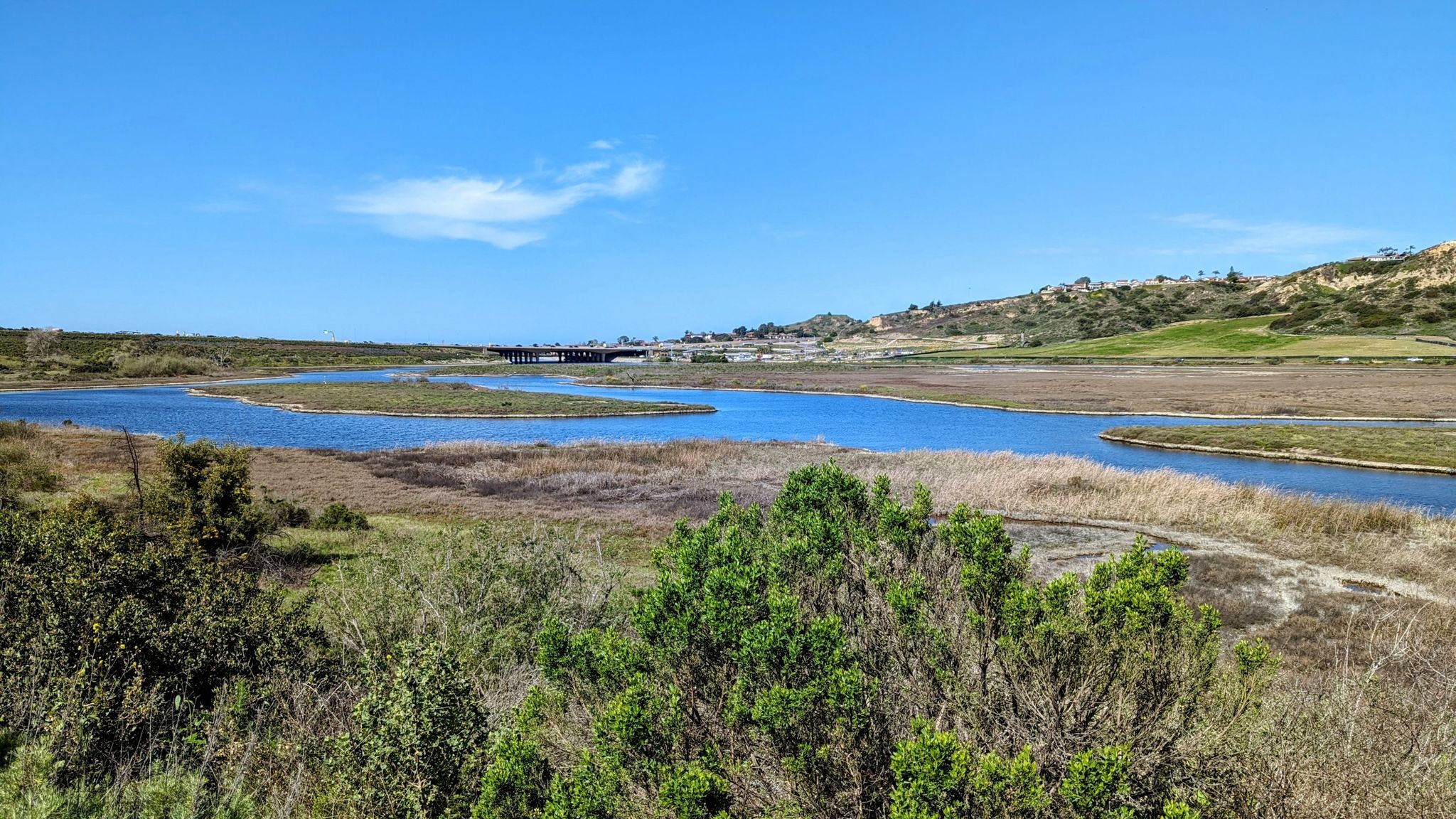 A wide blue river flows through a vast marshland under a clear sky. - Santa Inez to Santa Carina Loop Trail