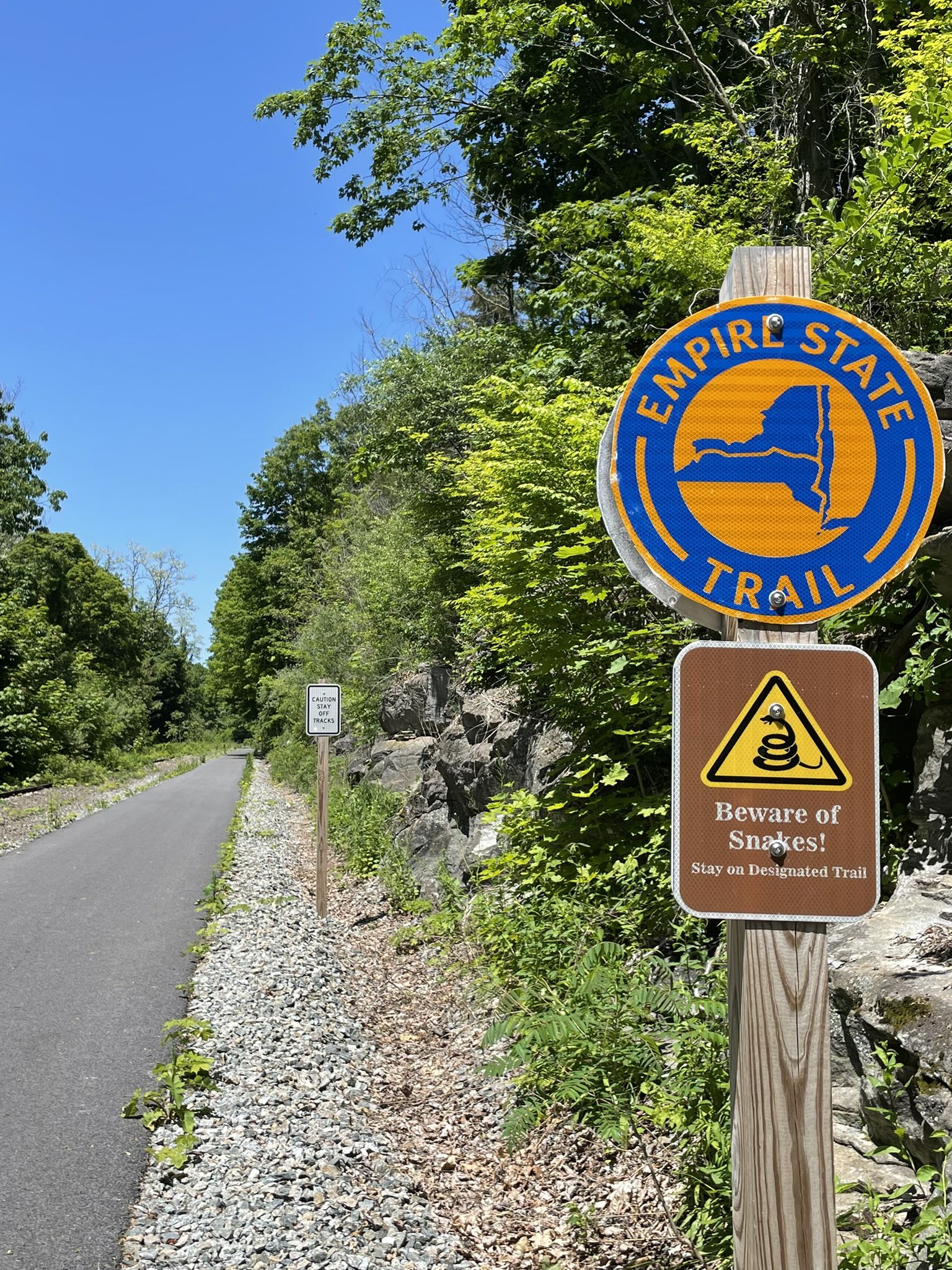 Trail signs on a wooden post next to a paved path and rocky hillside. - Maybrook Trailway loop from Beacon Line MT1