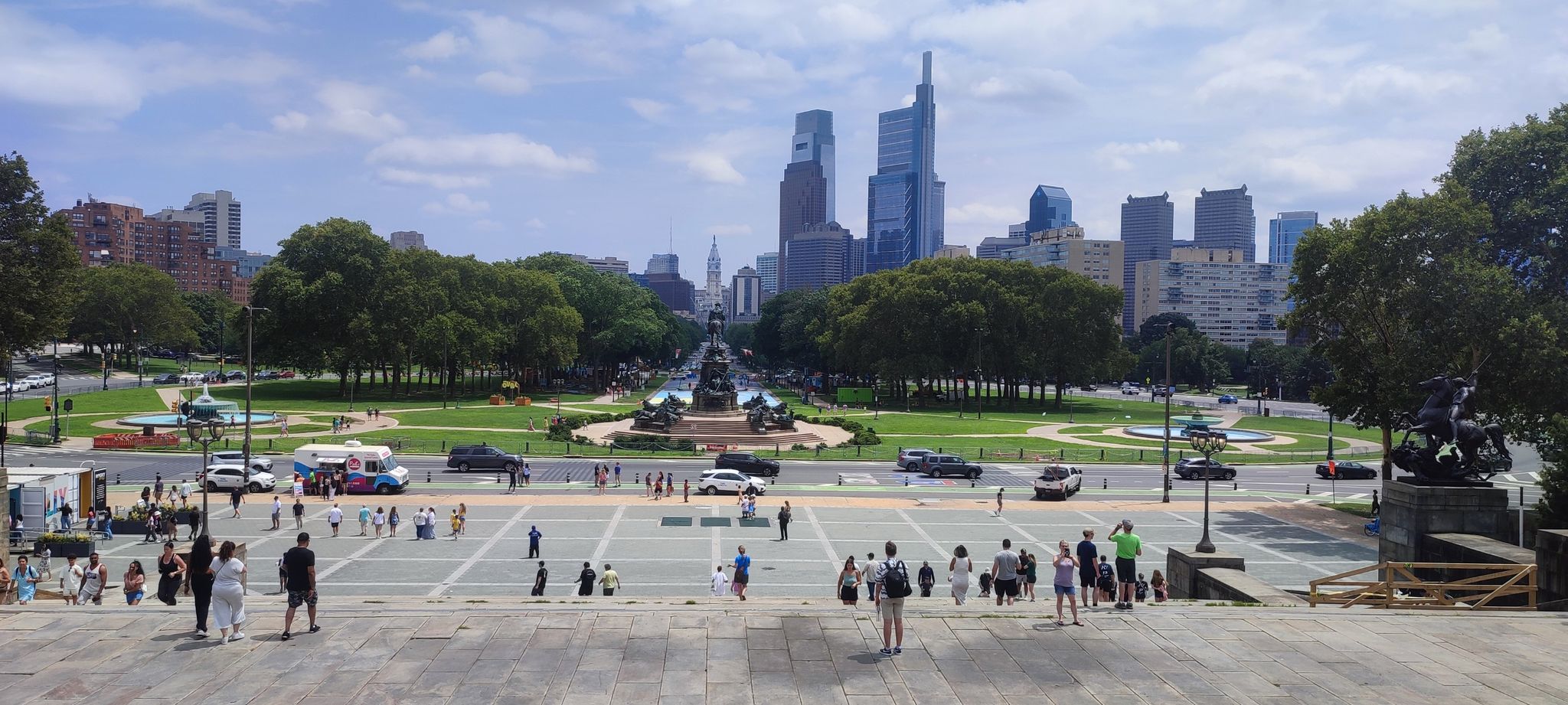 Crowd of people in a plaza overlooking a park and distant city skyline. - Rocky Statue – LOVE Sculpture, Love Park loop from Philadelphia