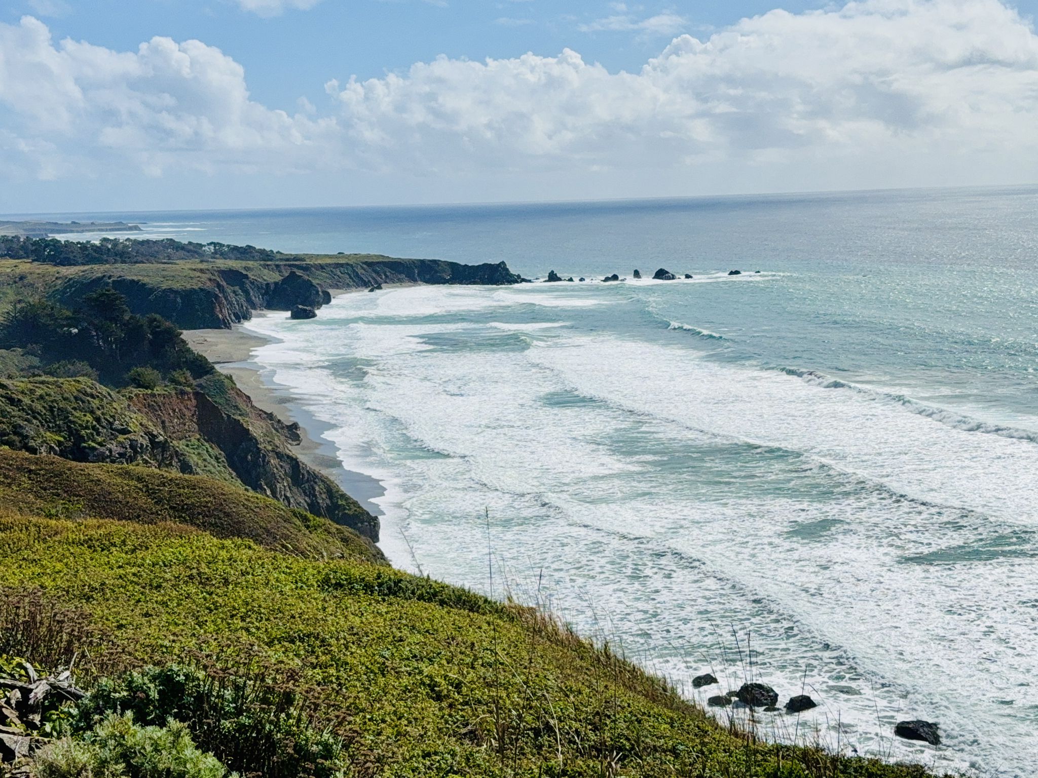 Cloudy coastal view with green bluffs and waves crashing on a beach. - Hearst Castle – Elephant Seal Vista Point loop from San Simeon