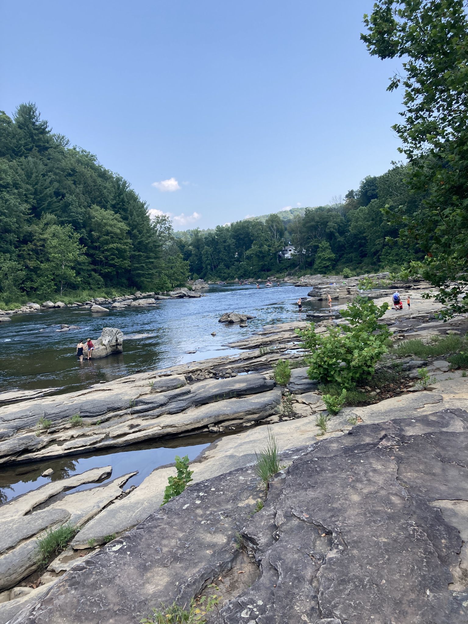 People wading in a wide river with rocky banks and distant forested hills. - Great Gorge and Ferncliff Trail Loop