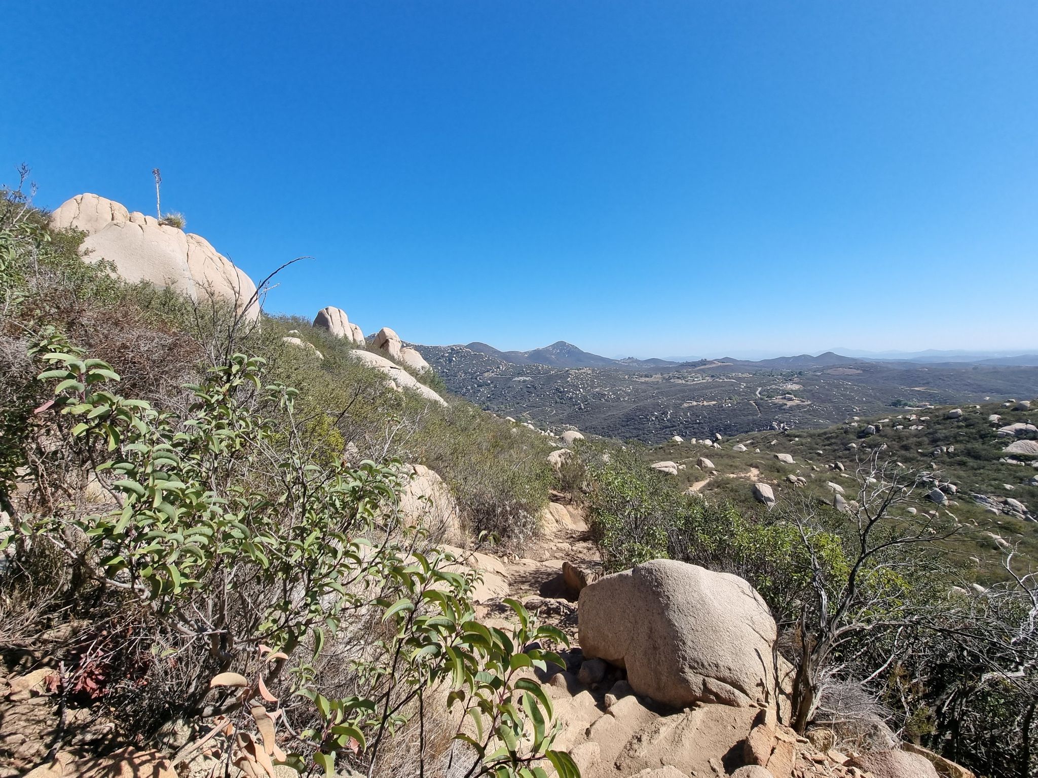 Rocky hillside trail with distant mountains under a clear blue sky. - Mount Woodson Trail